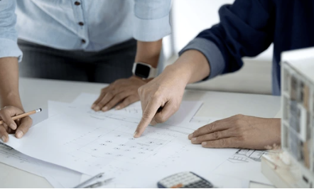 Two people reviewing and pointing at architectural plans or blueprints on a table.