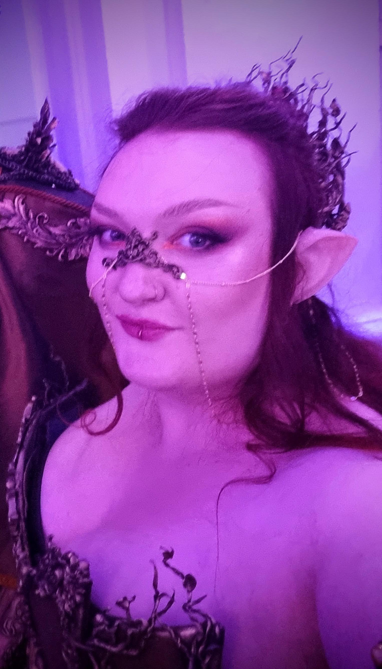 A woman with dark curly hair looks with longing out of a ruin window dressed in a flowy shirt and corset