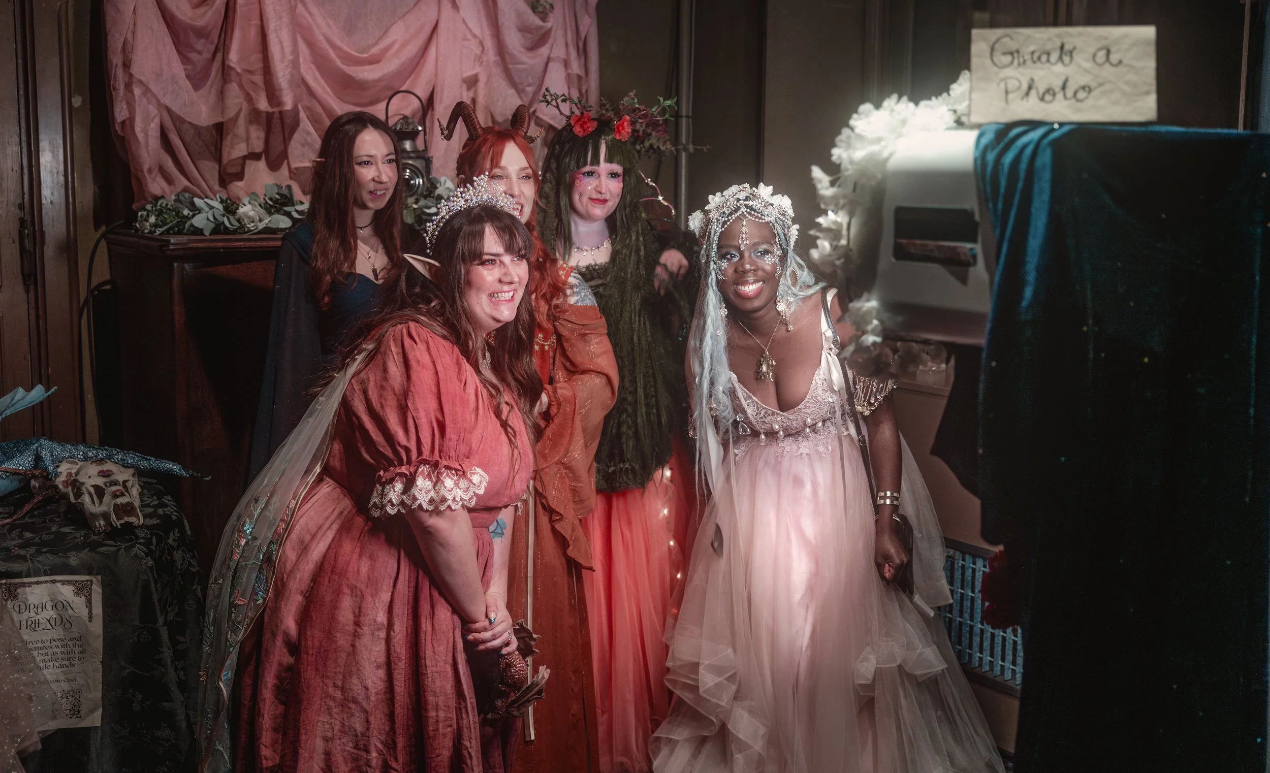 Group of women in costume taking a photo with a photo booth setup at a party or event, with a sign that says 'Great a Photo' in the background.