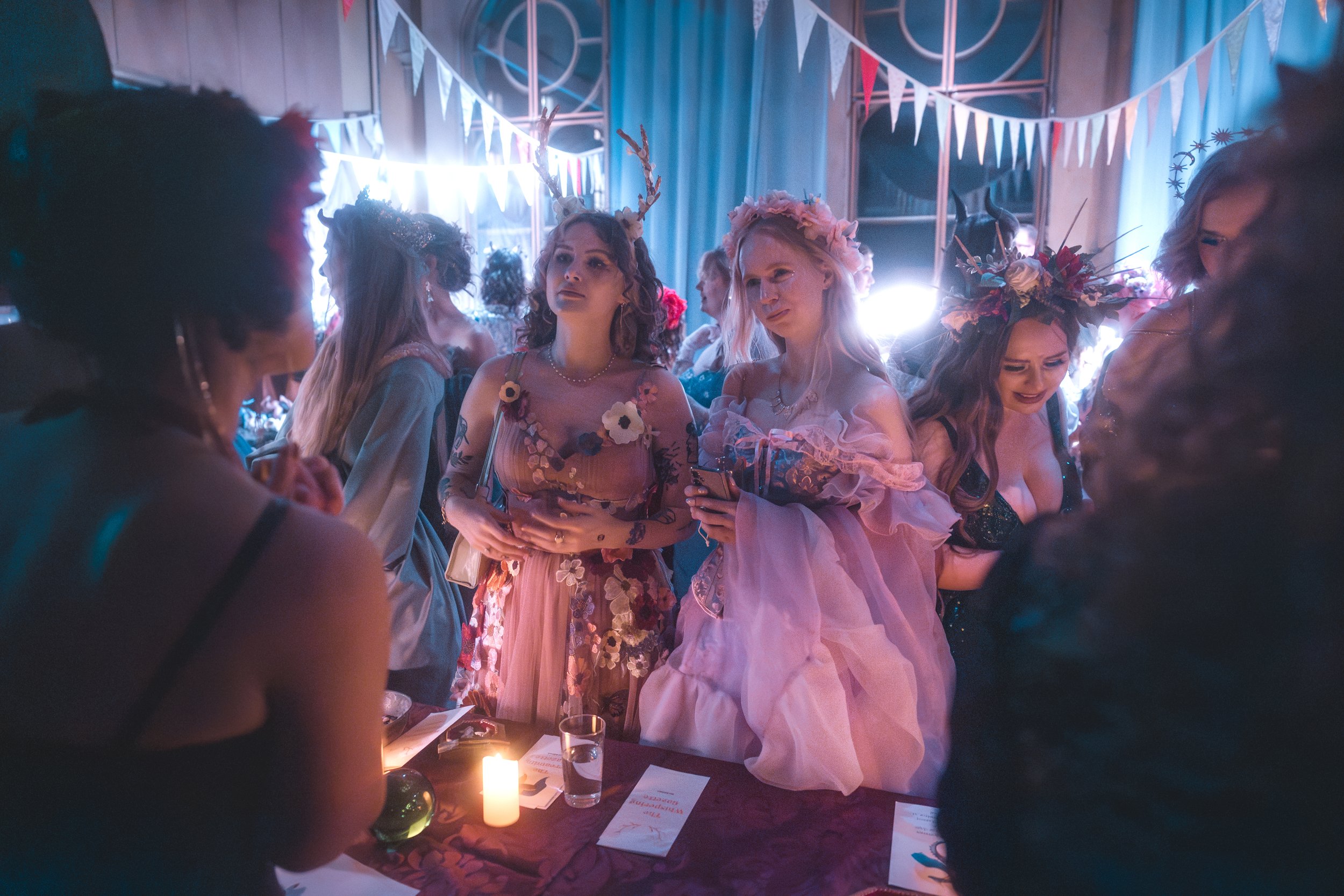 Group of people dressed in whimsical costumes at a party, decorated with bunting and festive lighting.