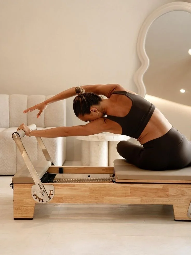 Frau macht eine Dehnübung auf einem Pilates-Reformer in einem Wohnzimmer.