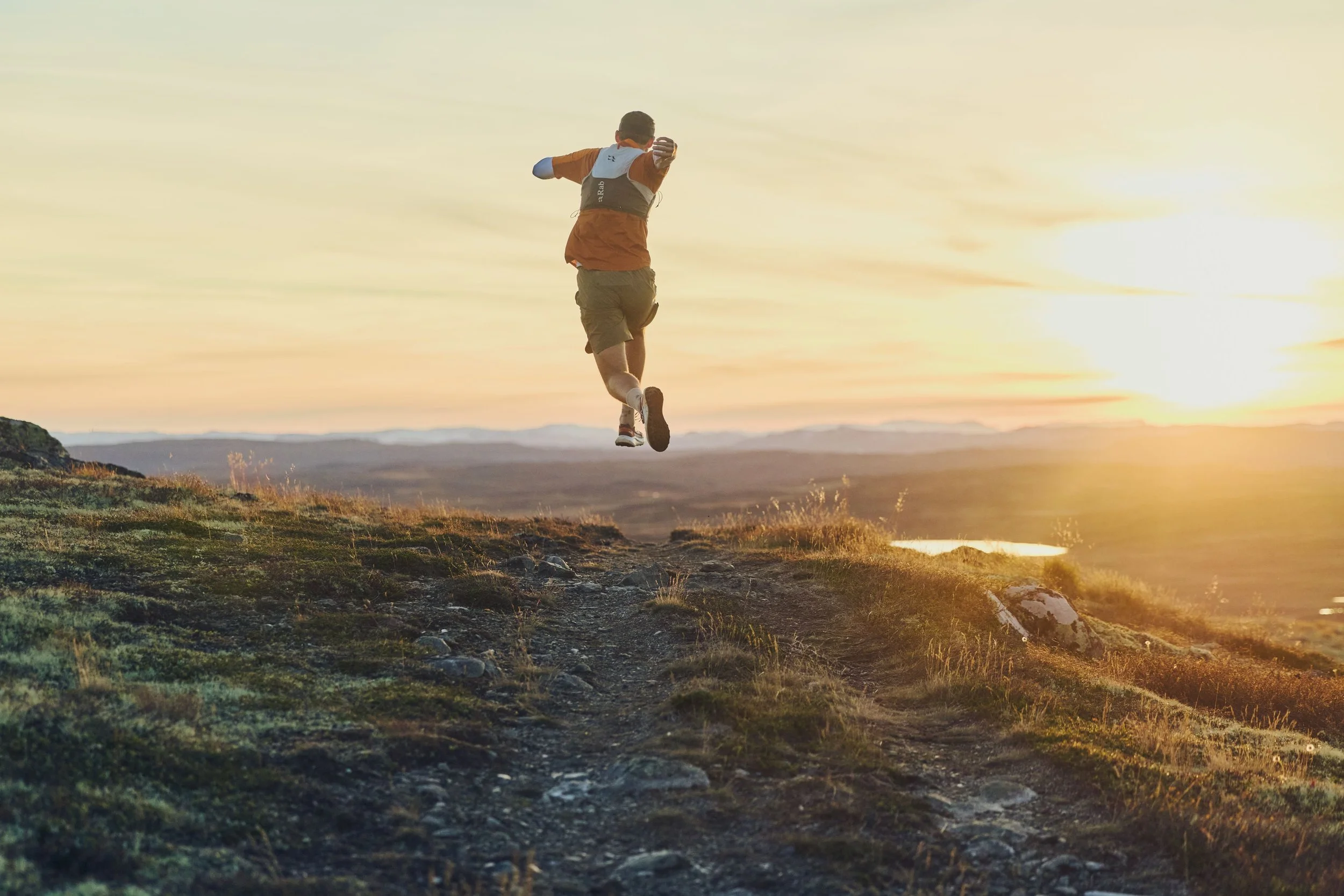 A person running on a dirt trail during sunset.