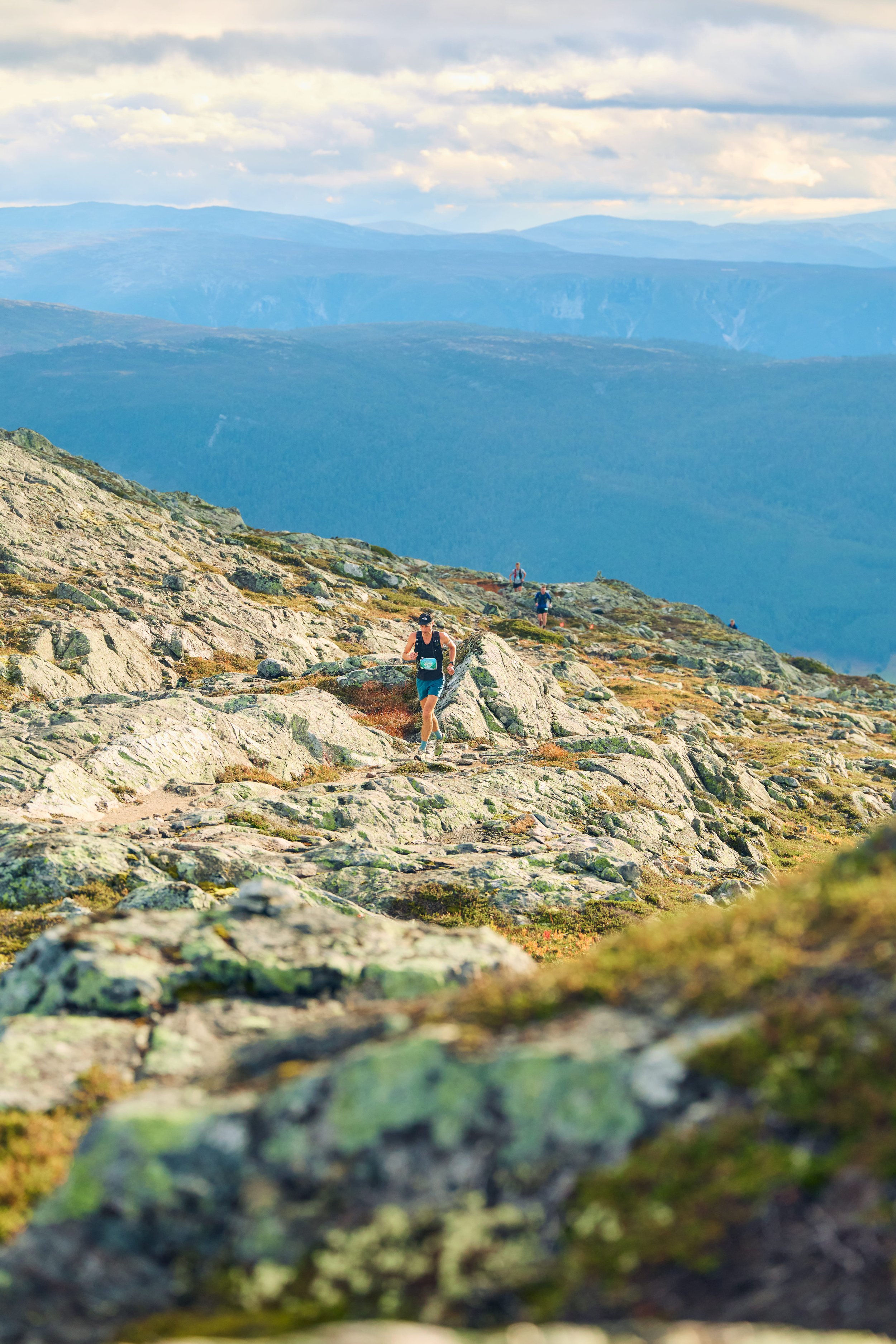 Hikers walking on rocky mountain trail with mountain landscape in background.