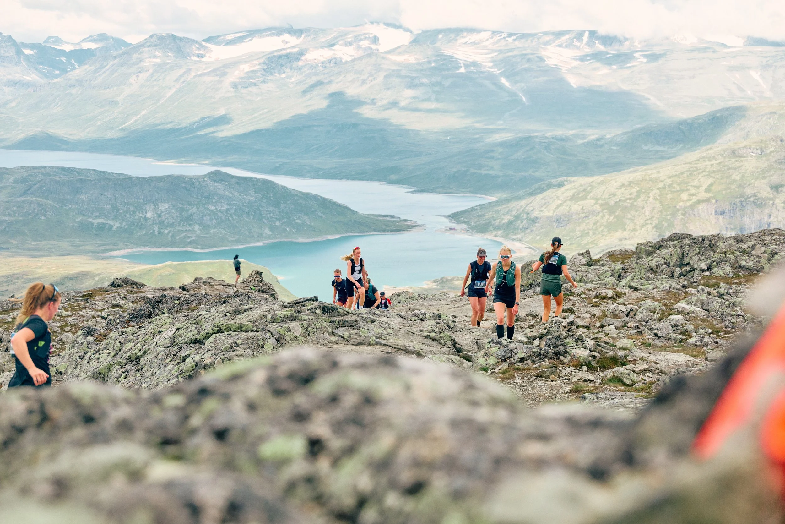 A group of hikers climbing on rocky terrain with a scenic view of lakes and mountains in the background.