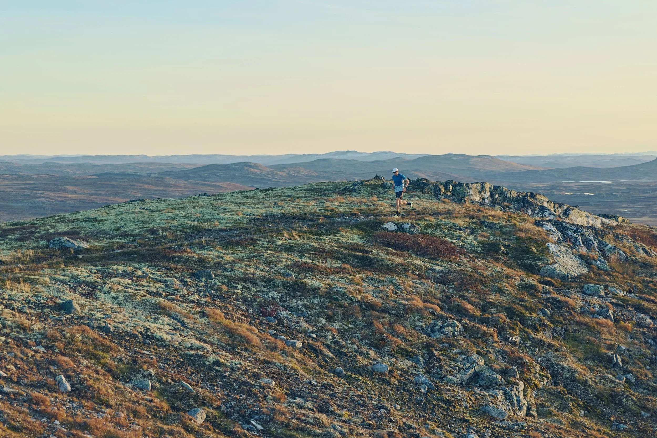 A person running on a rocky mountain ridge with a vast landscape in the background during sunset or sunrise.