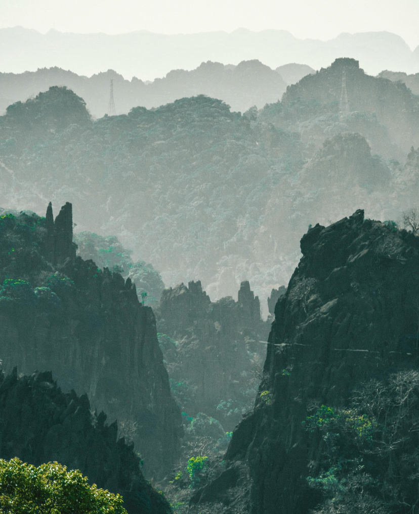 A layered view of misty mountain peaks and cliffs with lush green trees on some slopes.