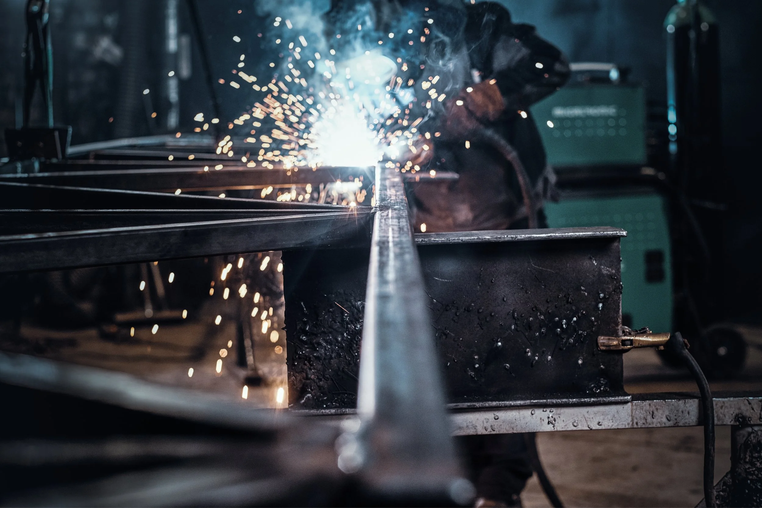 A person welding metal in a dark workshop, sparks flying around as the welding torch is applied.