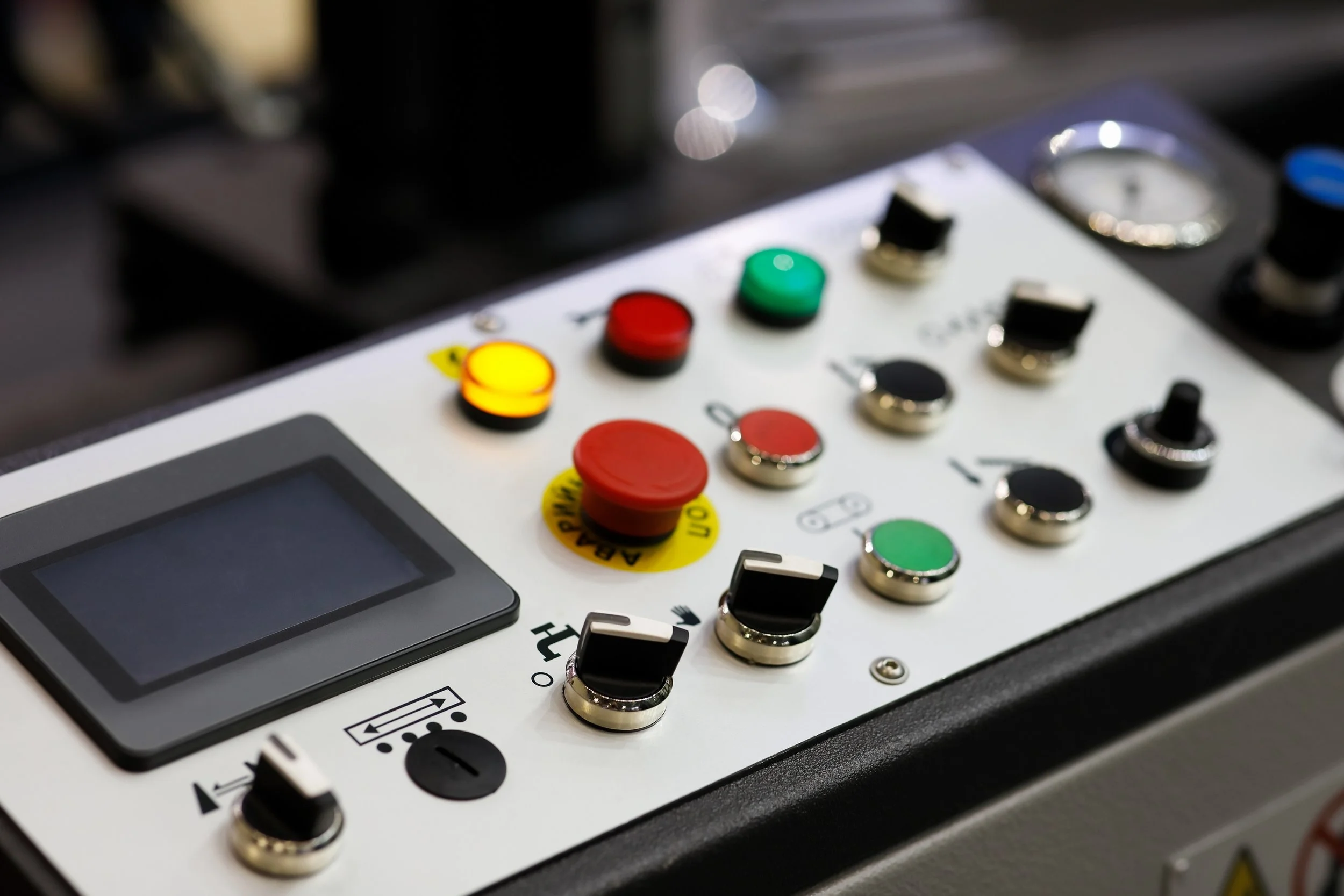 Close-up of a machine control panel with various colored buttons, switches, and a digital display screen.