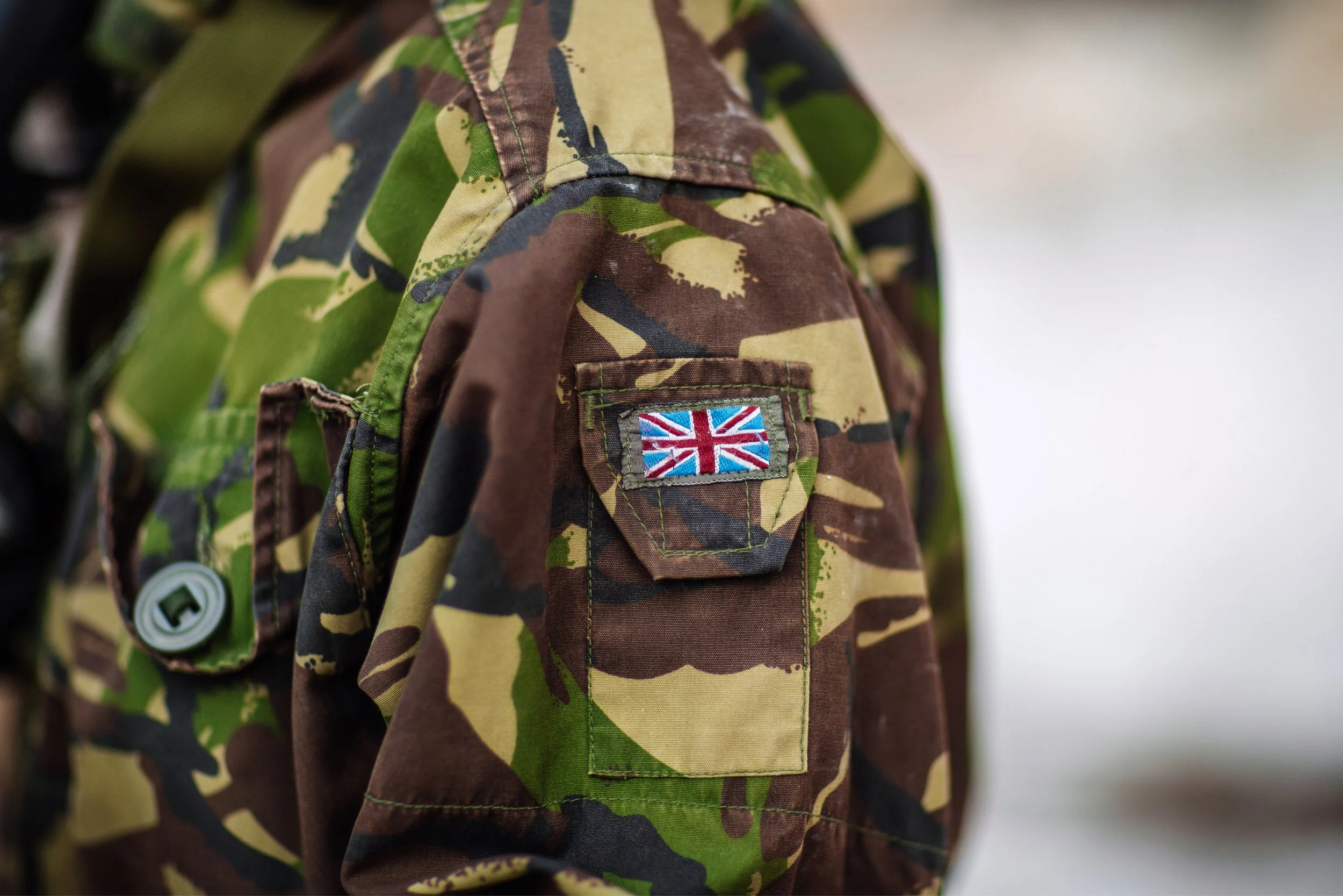 Close-up of a camouflage military uniform featuring a Union Jack flag patch on the sleeve.