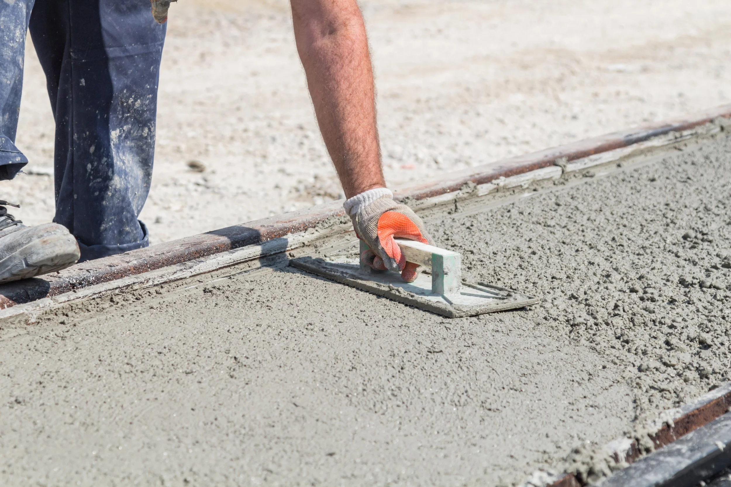 A worker smoothing wet concrete with a straightedge tool on a construction site.