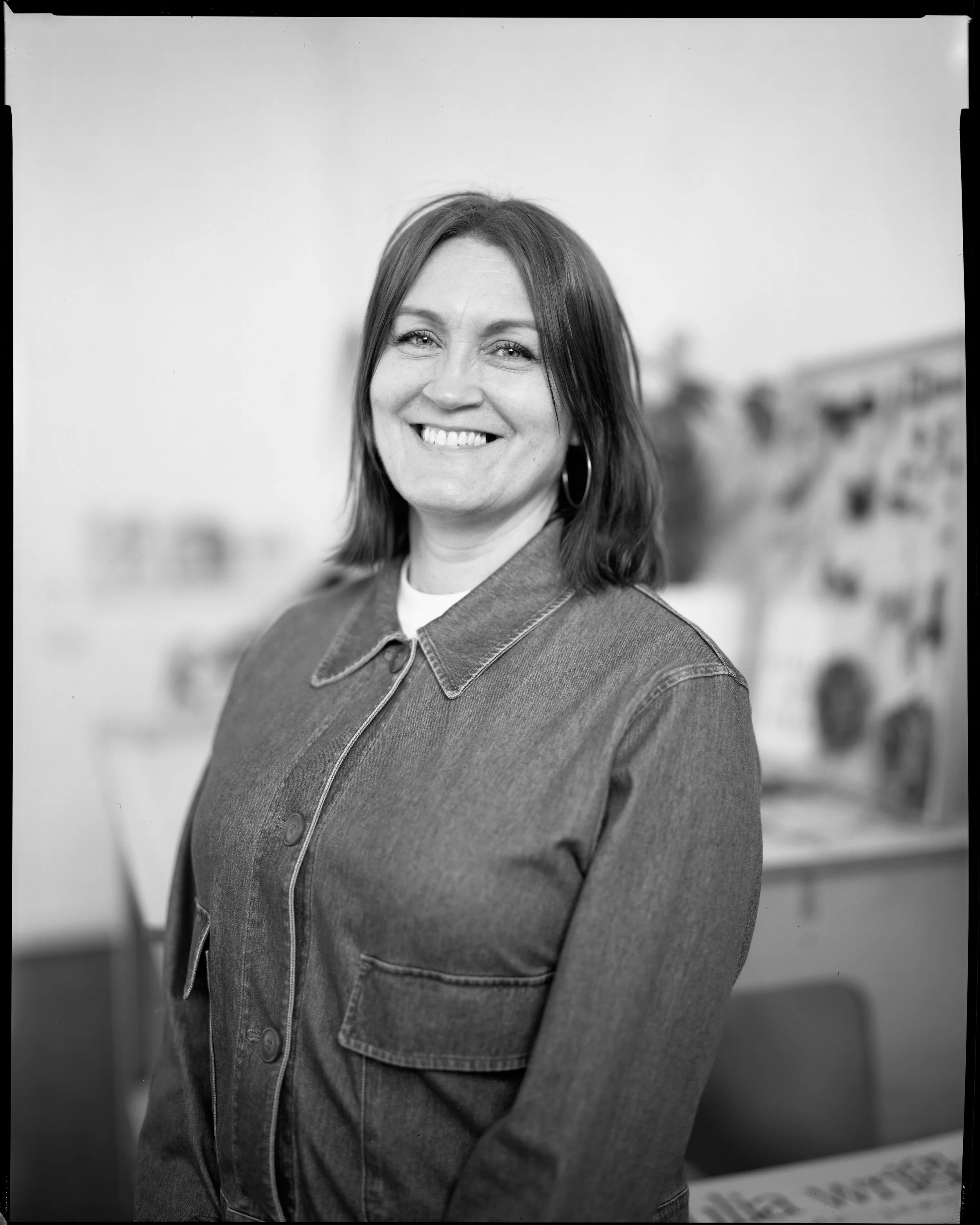 A woman with shoulder-length hair, wearing a denim jacket, smiling.
