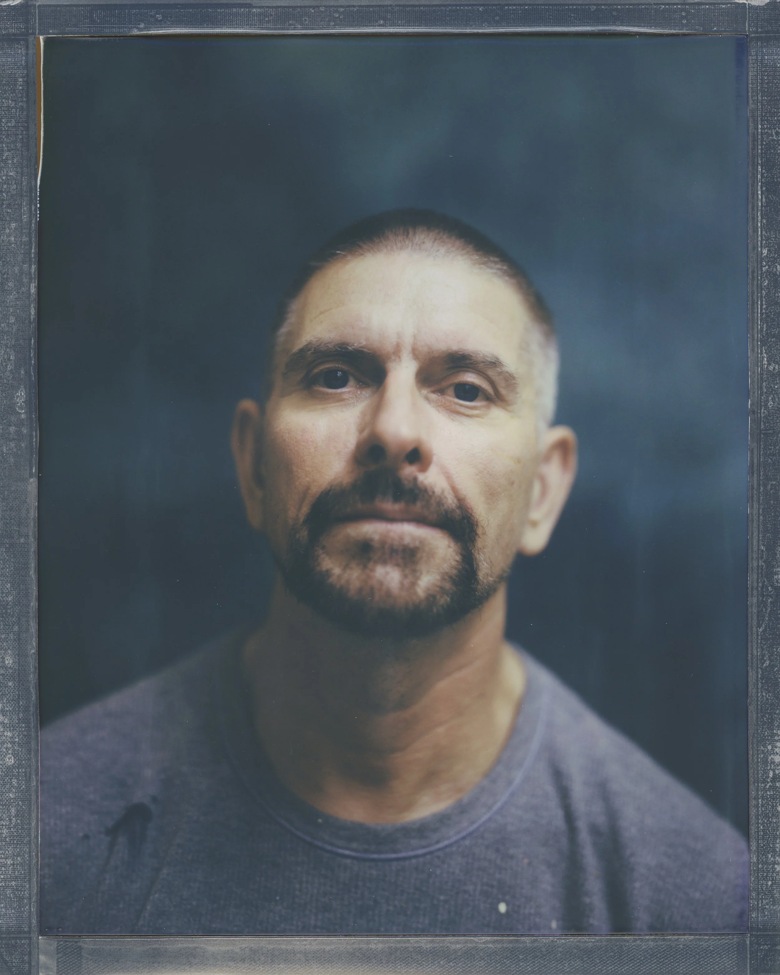 Close-up portrait of a man with short dark hair and a beard, looking directly at the camera.