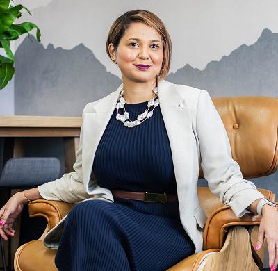 Woman sitting in a leather armchair with a neutral background and a plant to her side.