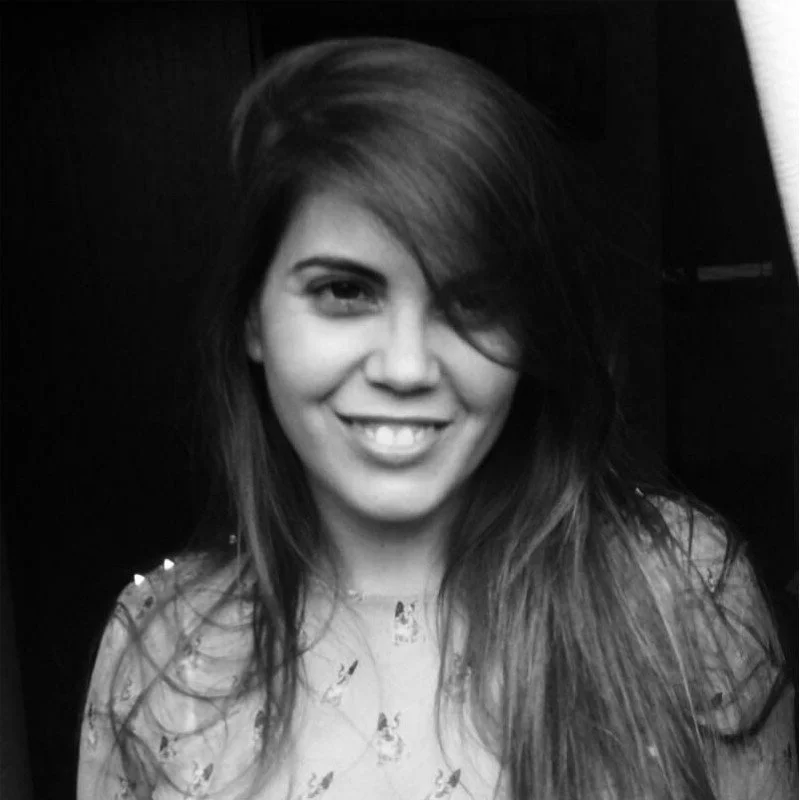 Rostro de una joven sonriendo, cabello largo y oscuro, en un fondo oscuro.