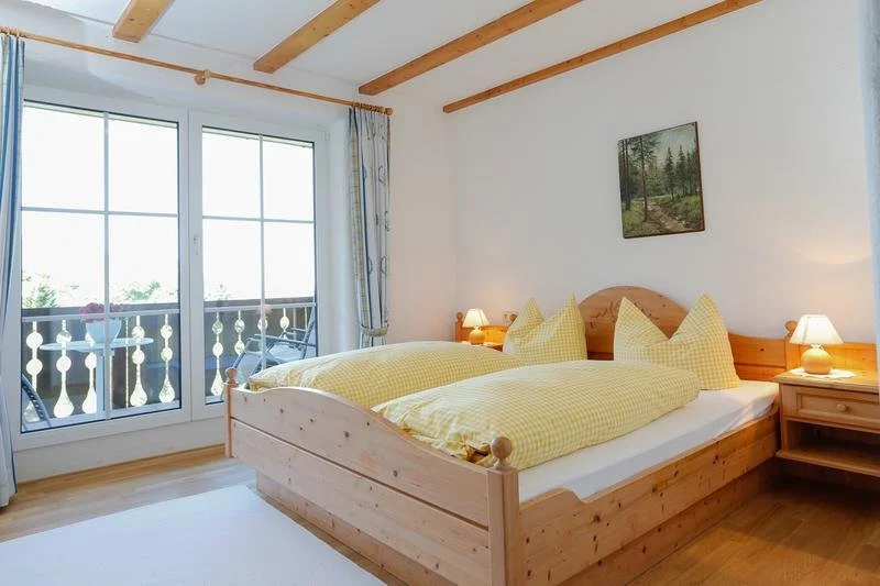 Schlafzimmer mit Doppelbett, gelben Bettdecken, Nachttischen mit Lampen, großer Fensterfront mit Balkon