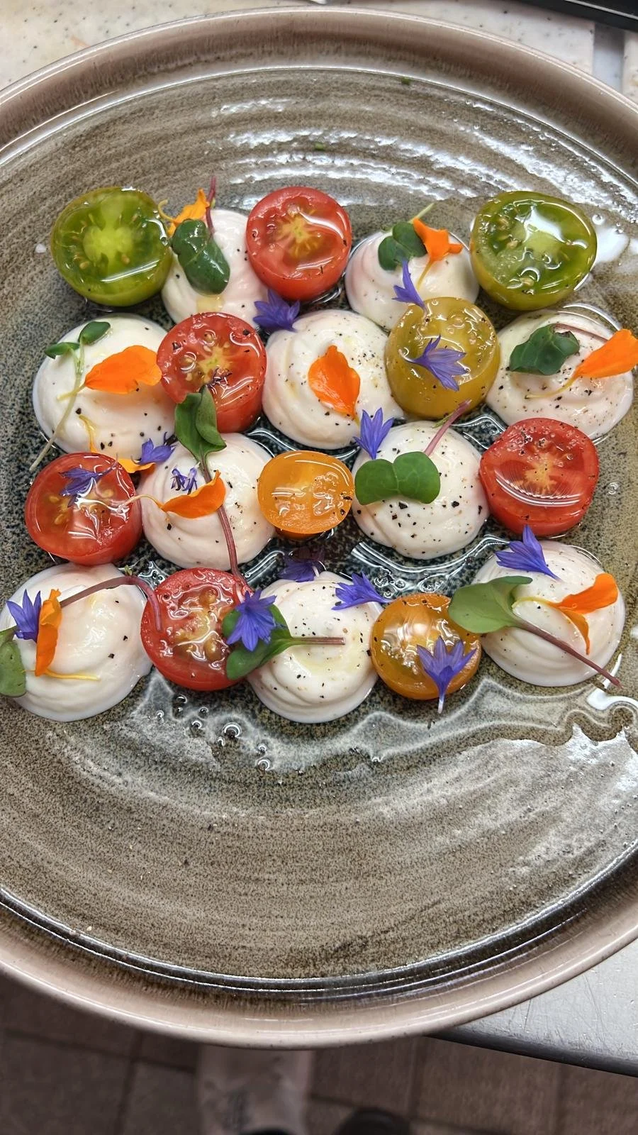 Mozzarella-Kugeln mit Kirschtomaten, frischen Kräutern und essbaren Blüten auf einer Platte