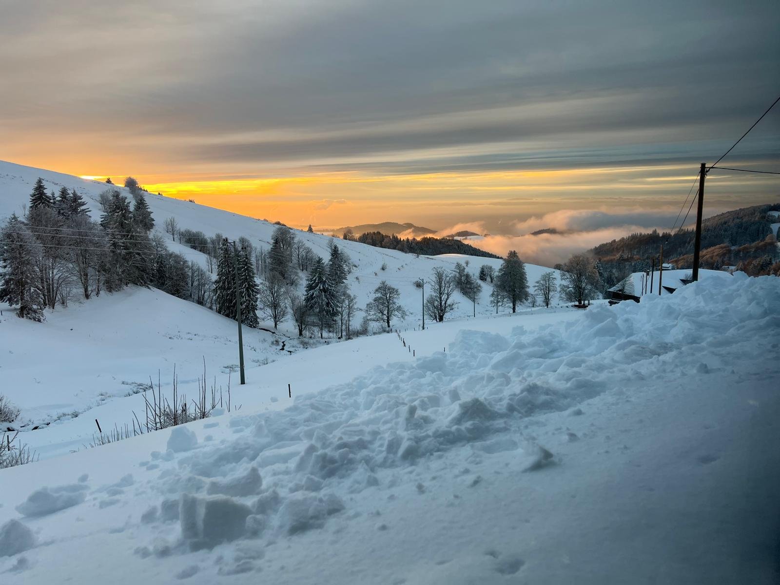 Eine verschneite Winterlandschaft mit Hügeln, Bäumen und einer schmalen Straße bei Sonnenuntergang oder Sonnenaufgang