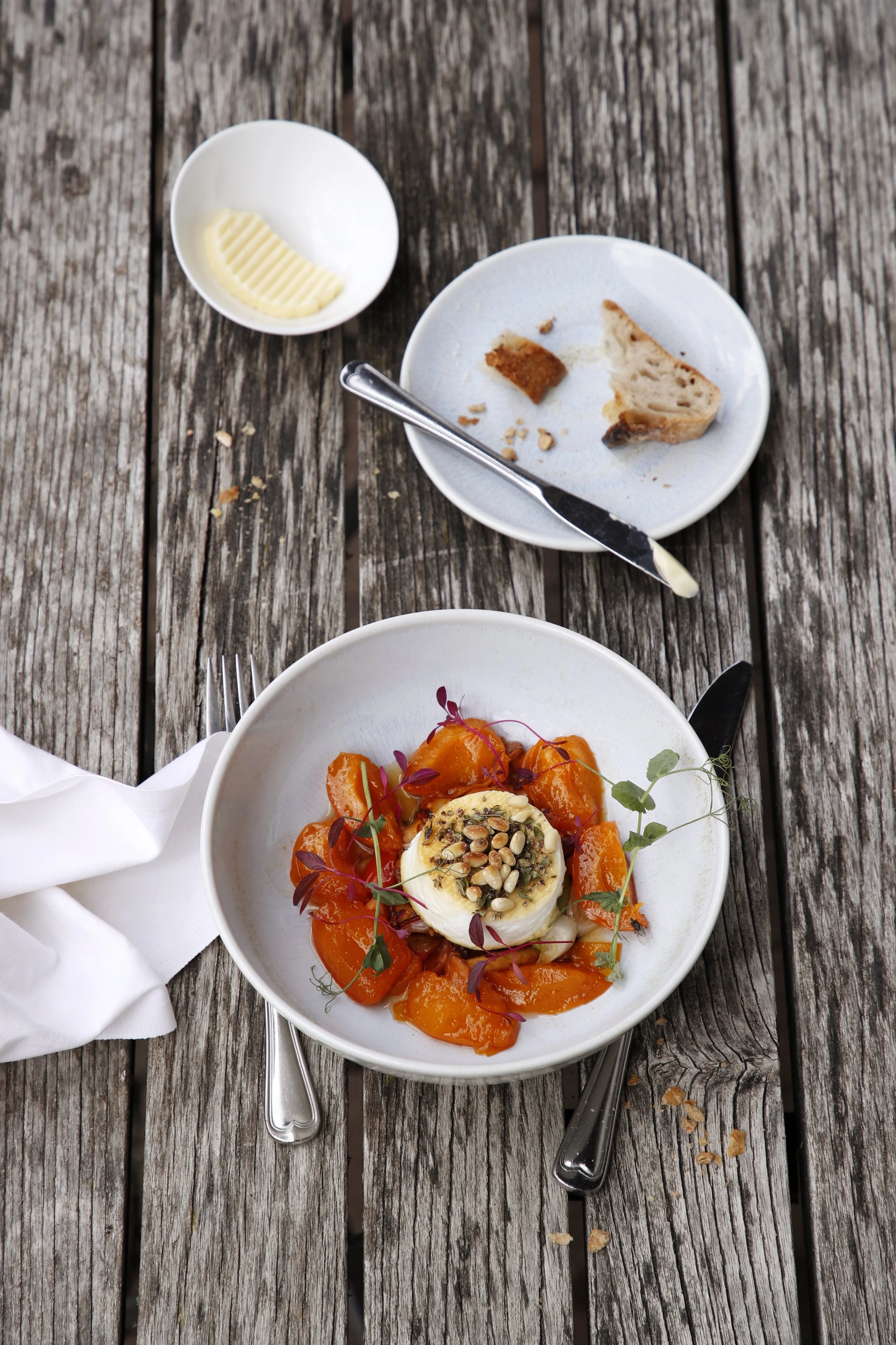 Ein leerer Teller mit, Wurst und ein Messer, ein kleiner Teller mit Butter, und ein leerer Teller mit einem Rest Stück Kuchen auf einem Holztisch.