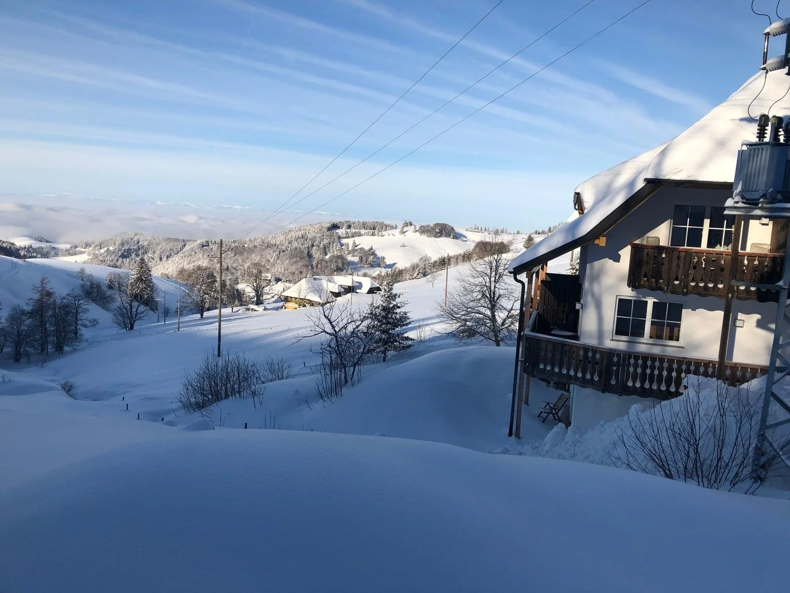 Ein verschneites Winterland mit einem traditionellen Chalet, Bäumen und Hügeln unter einem blauen Himmel.