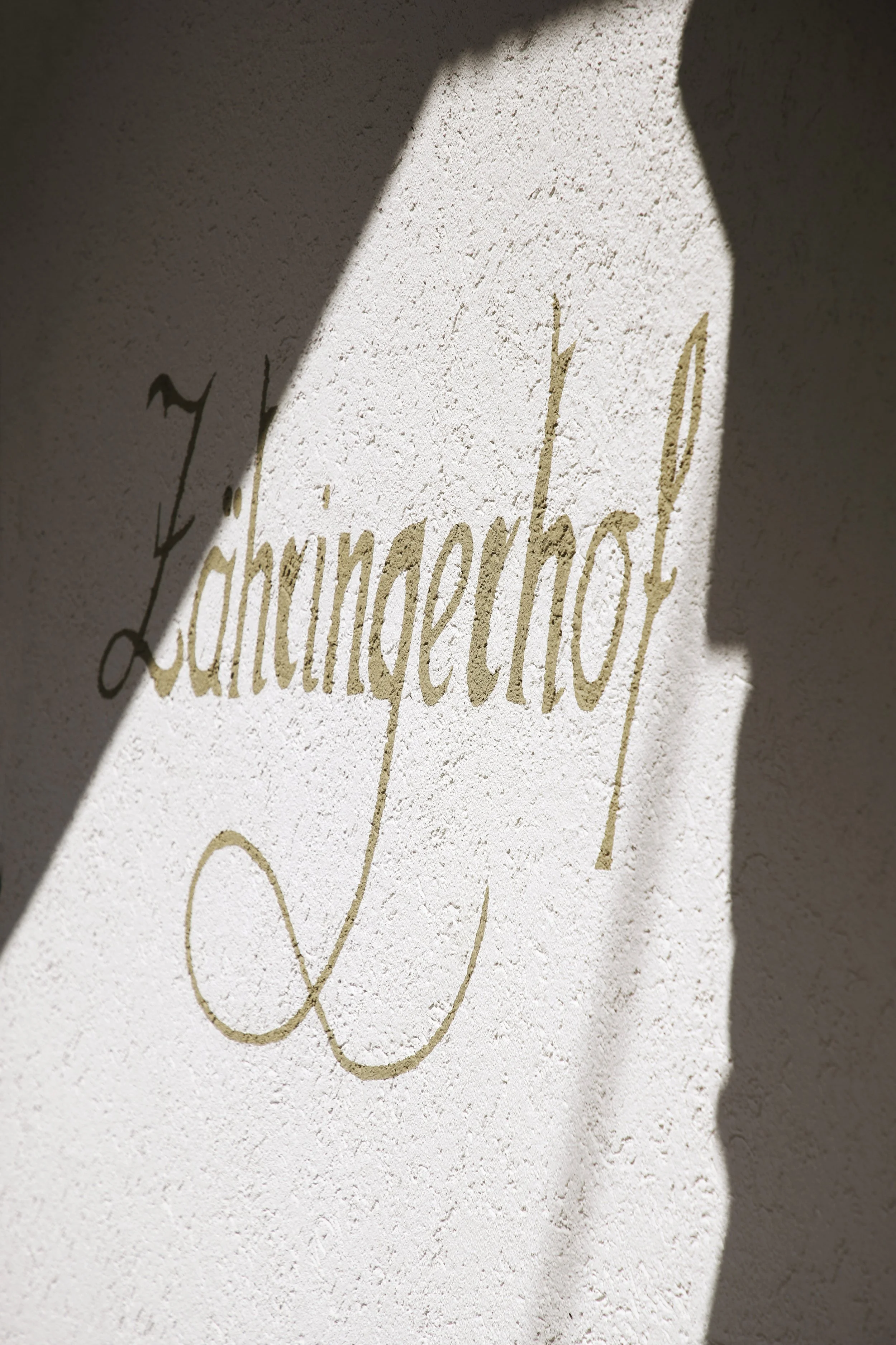 Ein Wandtext in Goldfarbe mit dem Wort 'Launaethol' auf einer weißen, strukturieren Wand, teilweise verdeckt durch Schatten.
