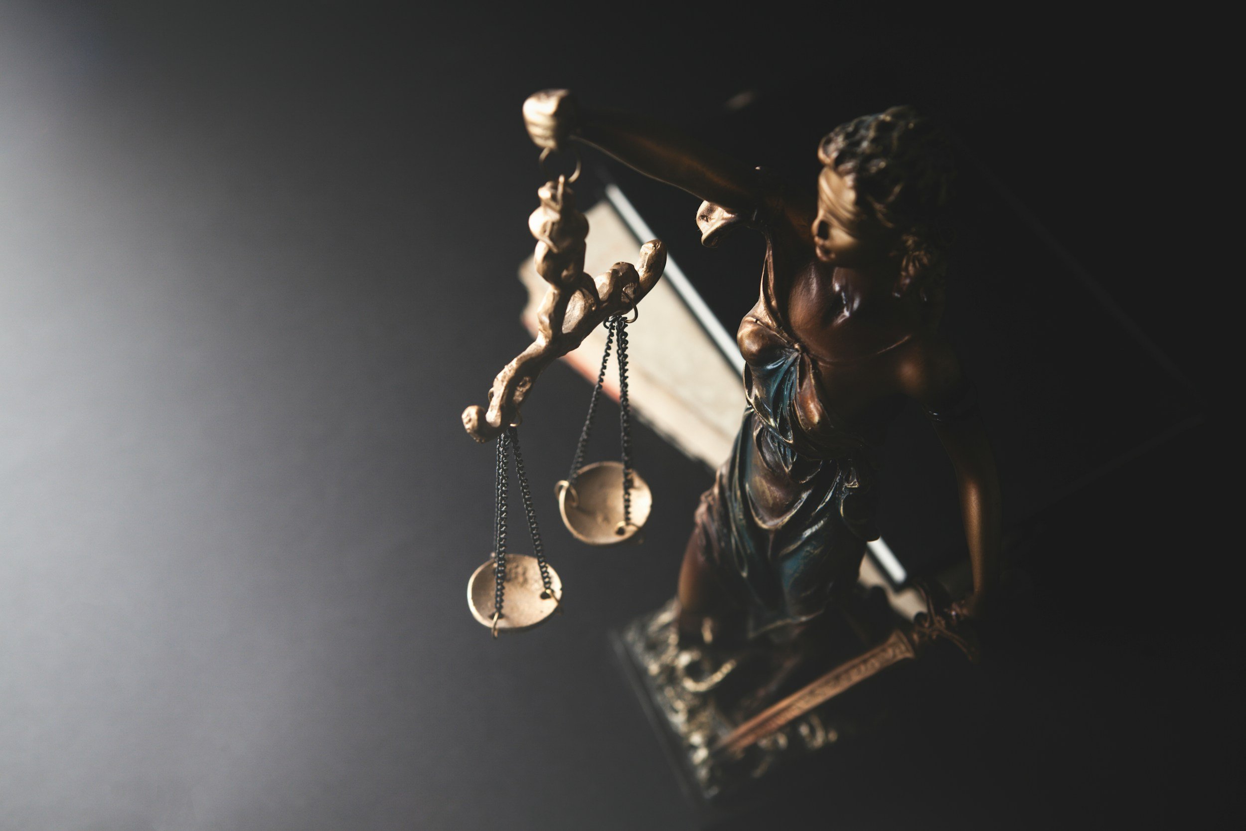 Statua della dea della giustizia con benda sugli occhi, bilancia e spada. Luce controllata su sfondo scuro.