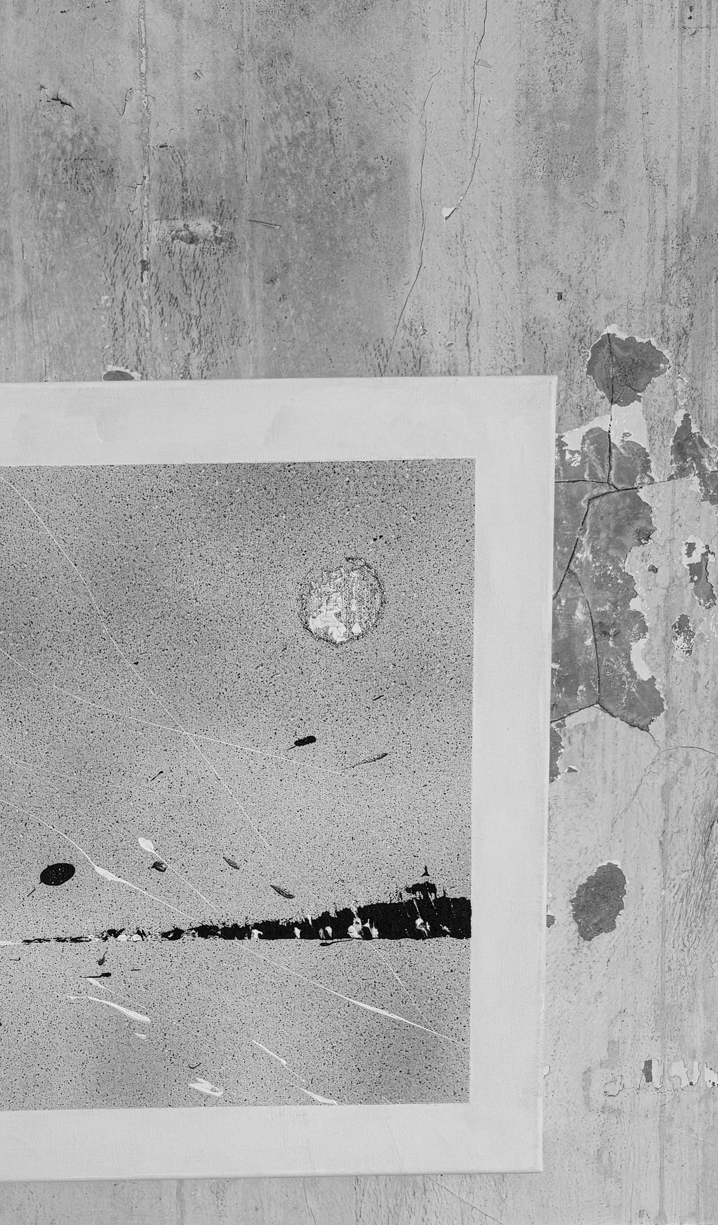 Black and white photograph of a textured surface, possibly concrete, with a printed or painted image of a small, round object and some scratches and marks on it, placed on a flat surface.