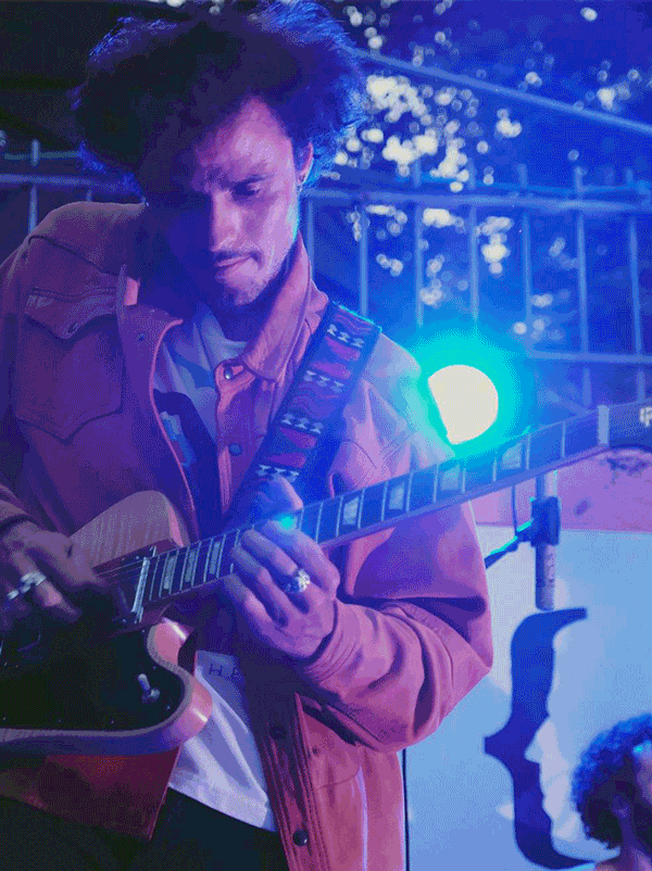 Un homme joue de la guitare électrique dans un environnement coloré avec des lumières bleues et violettes.