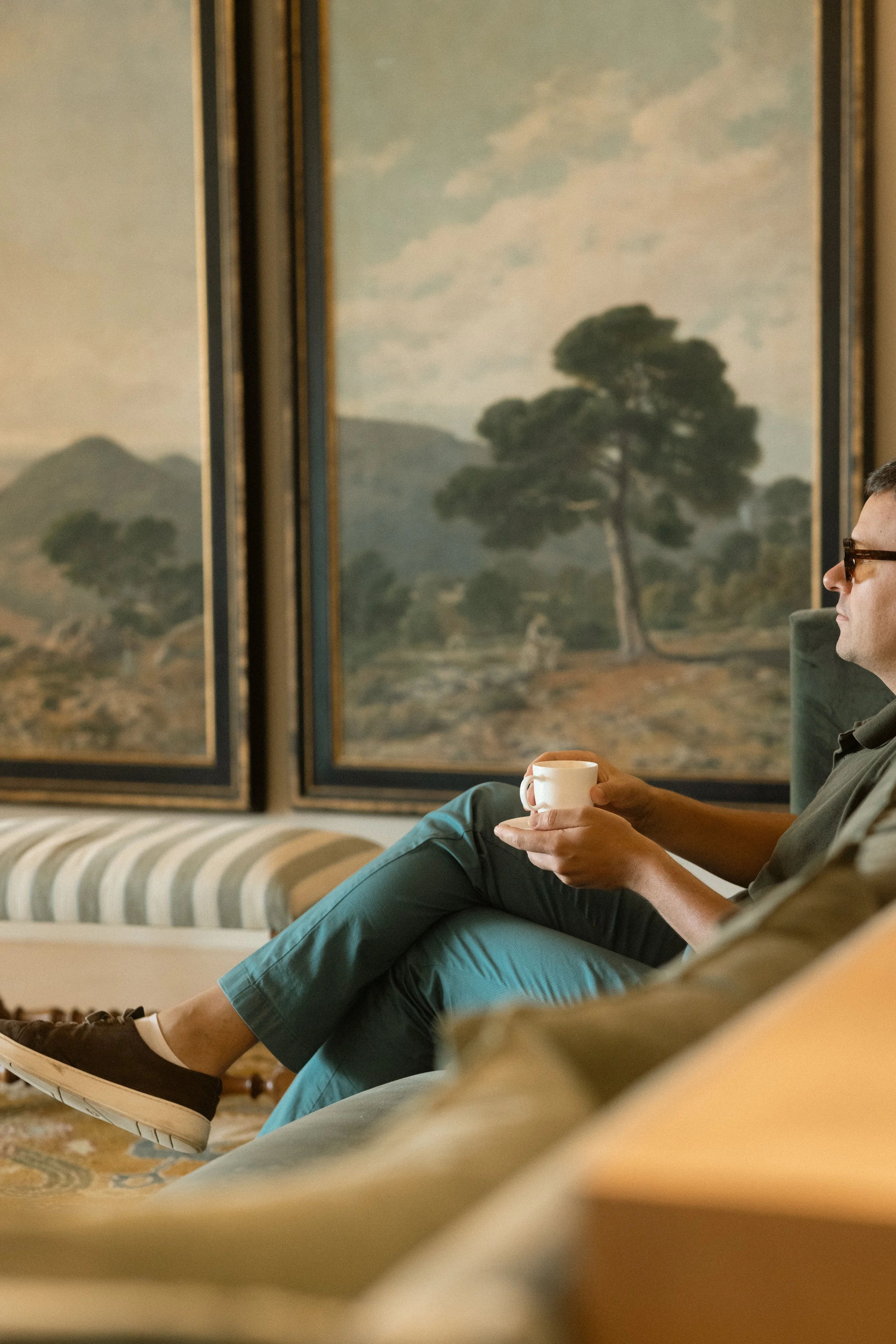 Art-inspired relaxation at Hotel Perelada: guest enjoying a coffee in a luxury lounge surrounded by curated landscape paintings.