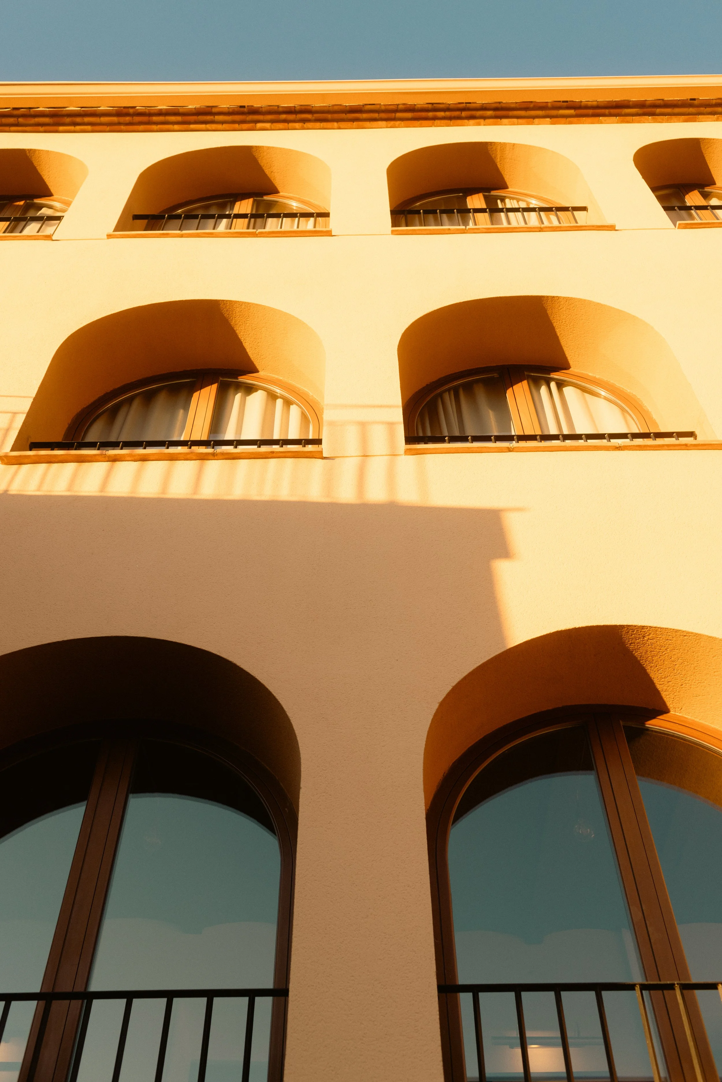 Exterior view of a traditional stone building with arched windows, wrought-iron balconies, and a warm-toned façade under a clear blue sky at Ora Priorat. Professional hotel and travel photography.