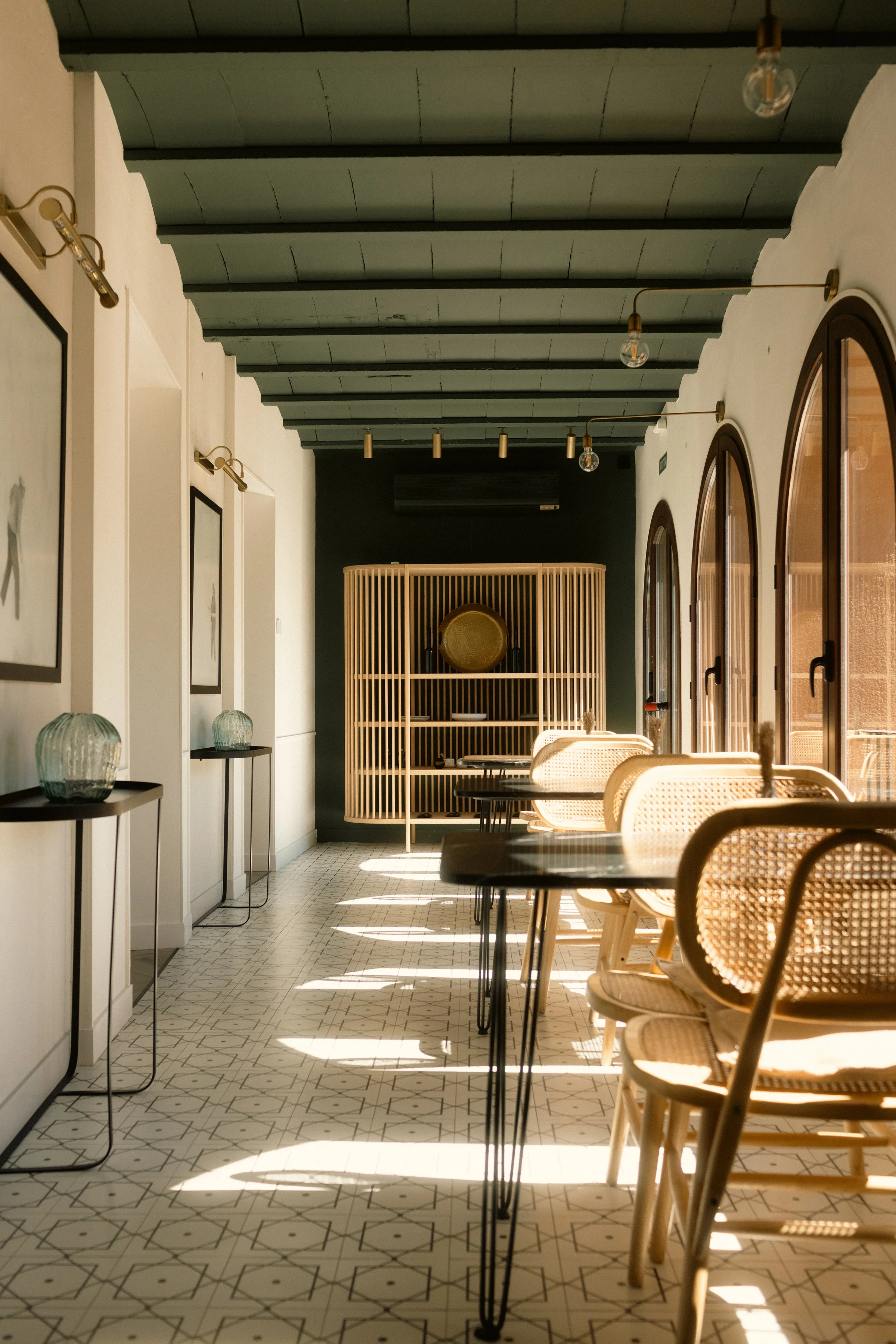 Restaurant interior photography: sunlit dining area with natural textures, wicker chairs, and architectural arched windows. Professional hospitality portfolio imagery at Ora Priorat.