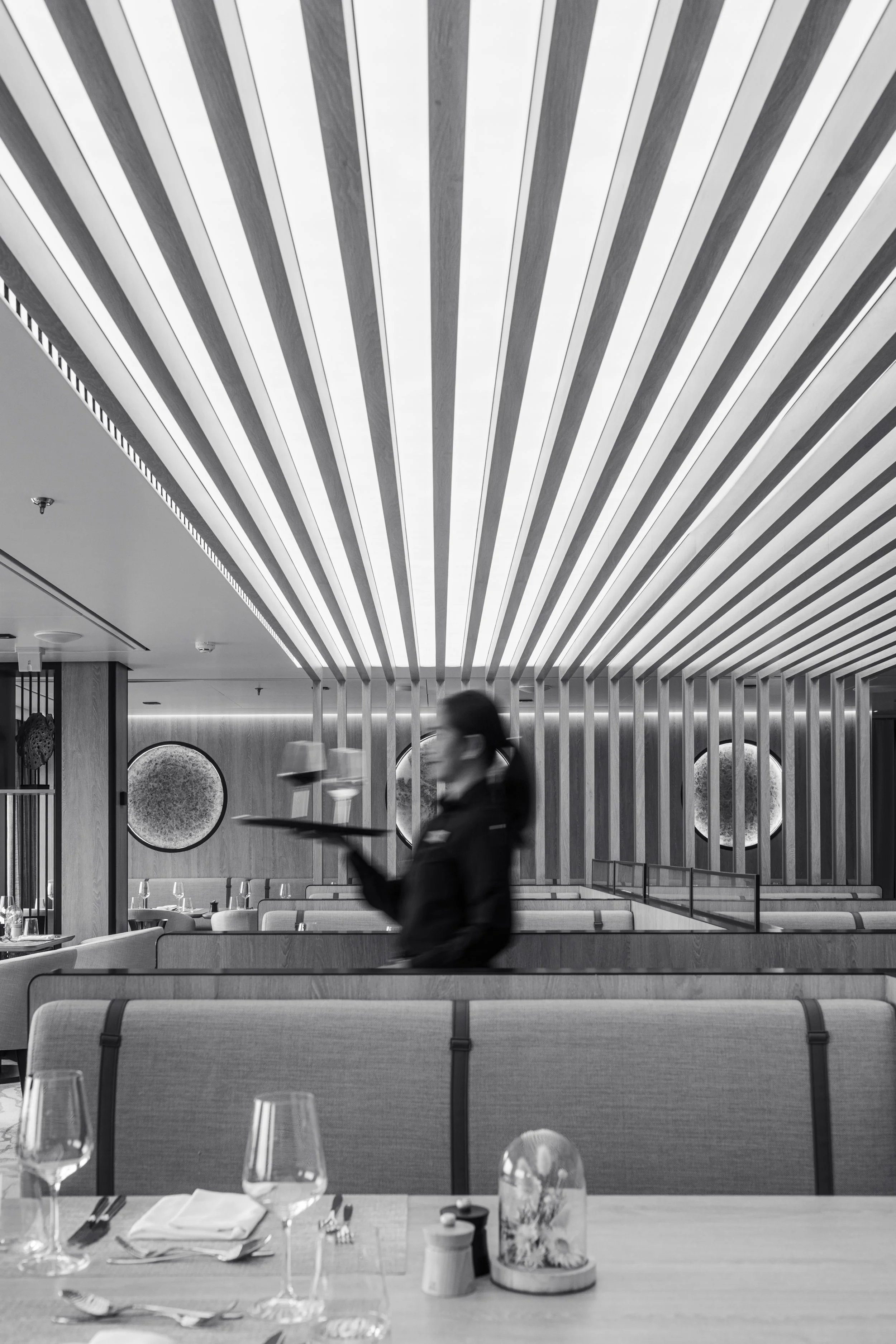 Swan Hellenic SH Minerva expedition cruise photography, restaurant interior with tables set for dining and crew member, black and white.
