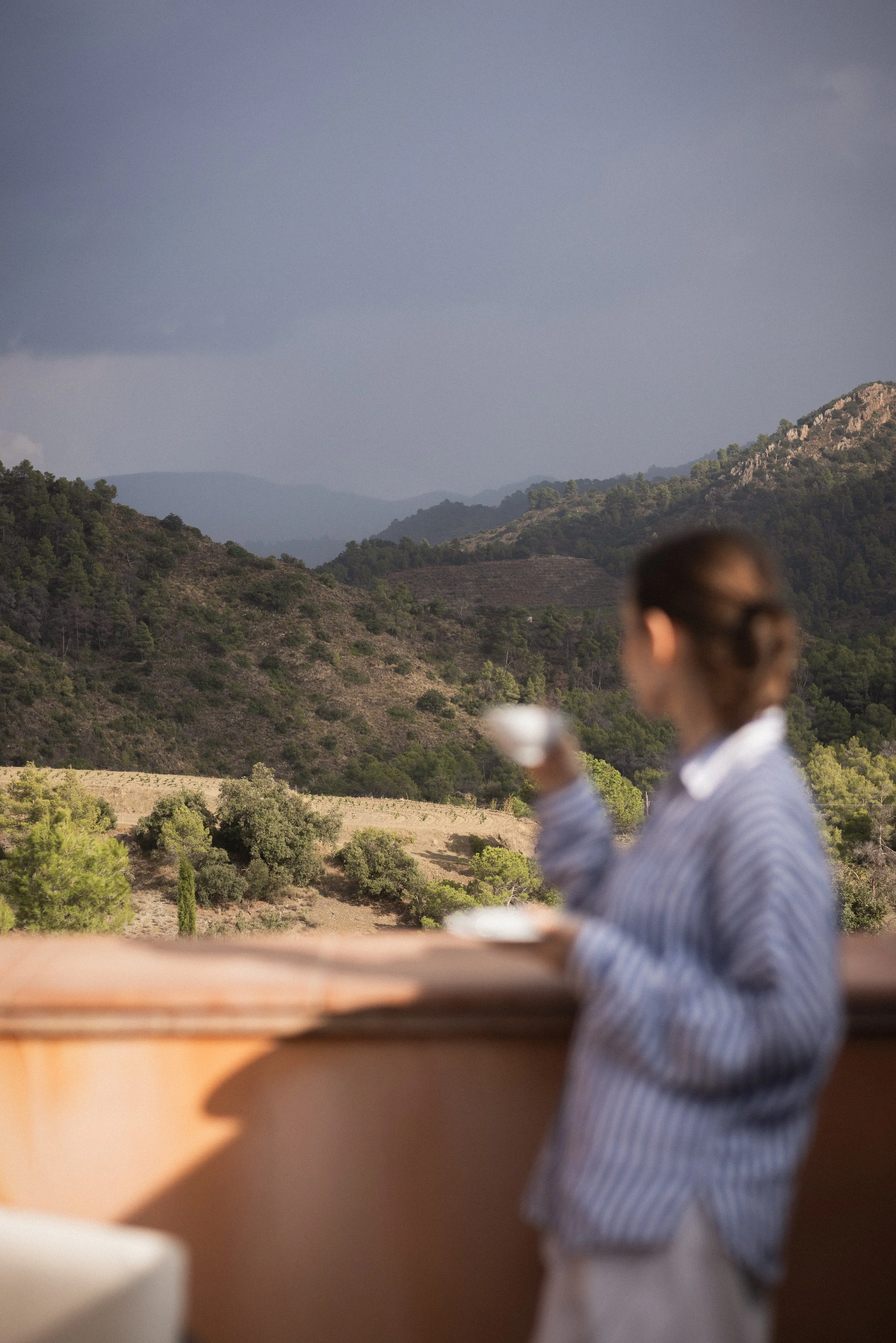 Mas d’en Bruno hotel lifestyle photography with mountain views and a guest enjoying a drink outdoors, Catalonia, Spain.
