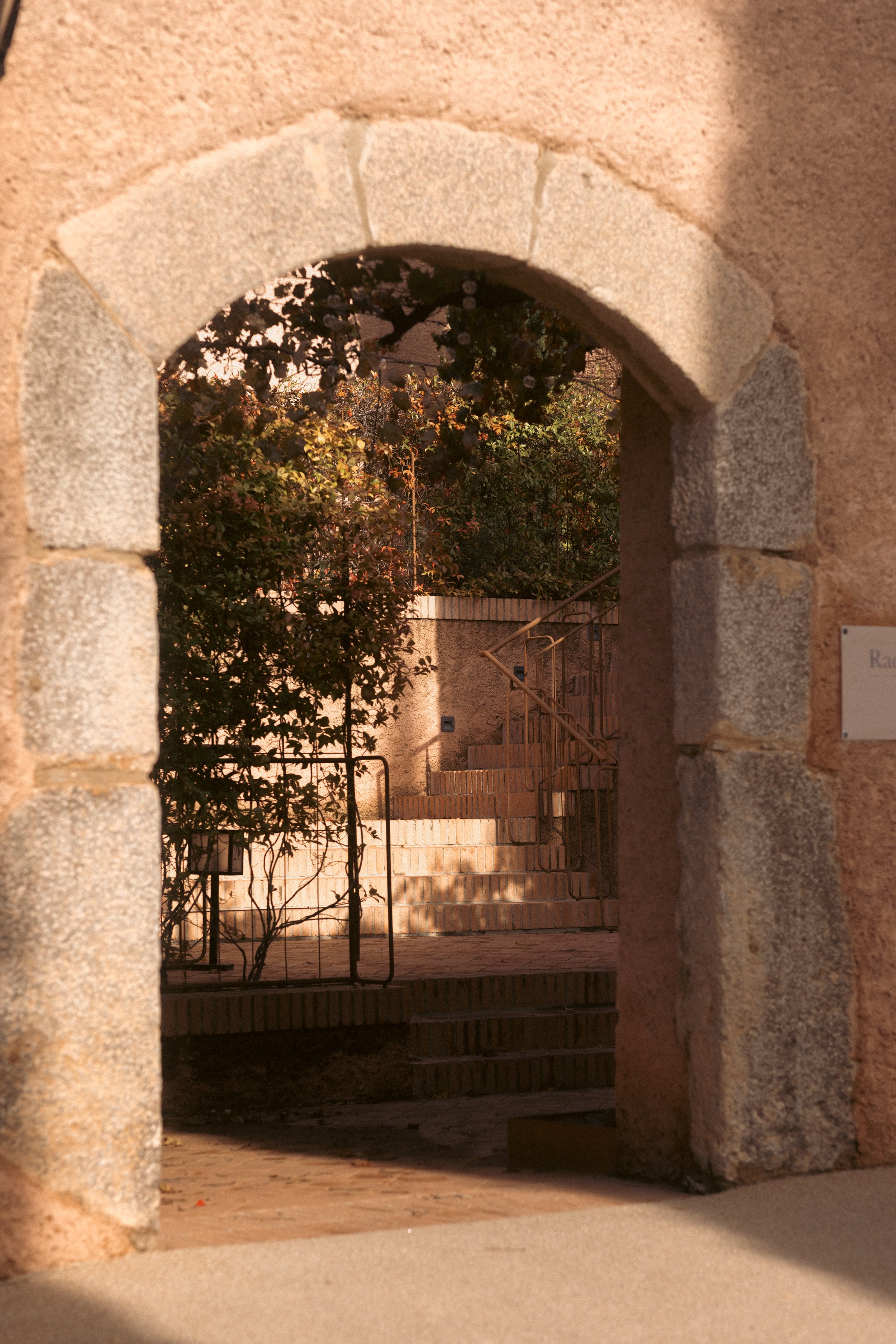 Historic elegance at Terra Dominicata: a sunlit stone archway leading through the tranquil Mediterranean courtyard of the Priorat estate.