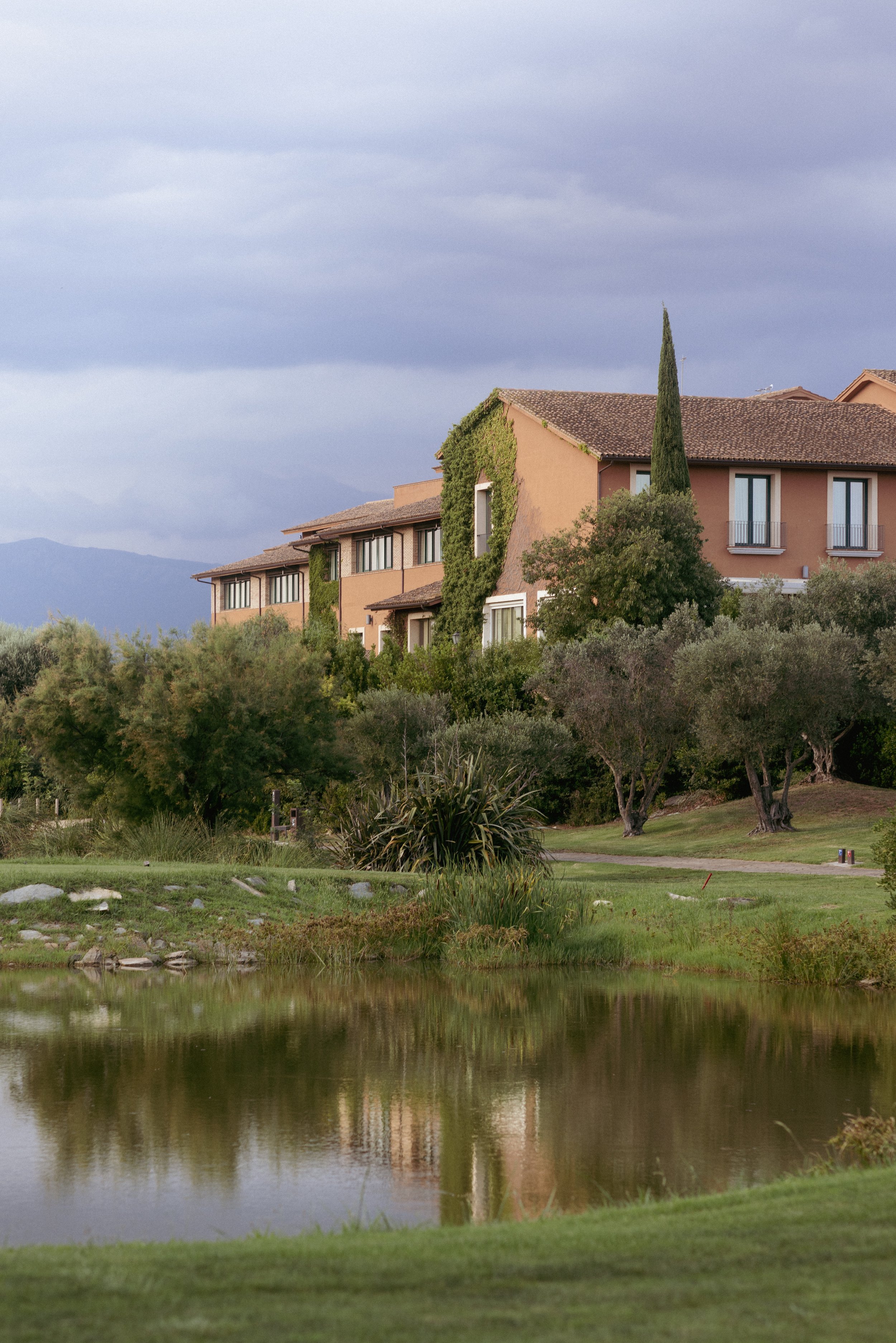 Serene Mediterranean architecture at Hotel Perelada: resort suites and lush greenery reflected in a tranquil pond.
