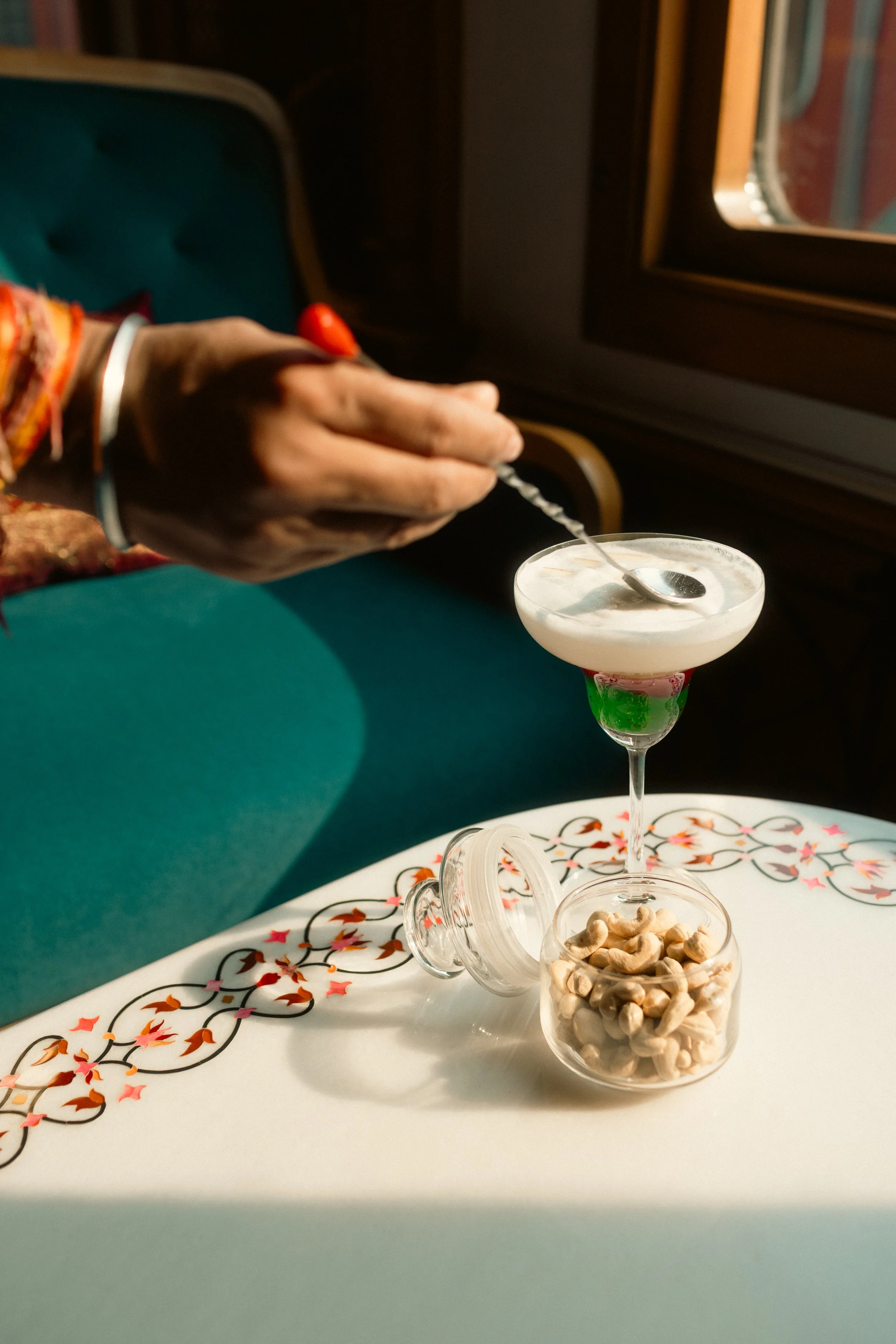 Food and beverage photography: Close-up of a bartender garnishing a layered cocktail with a cherry. Professional hospitality portfolio imagery at Deccan Odyssey.