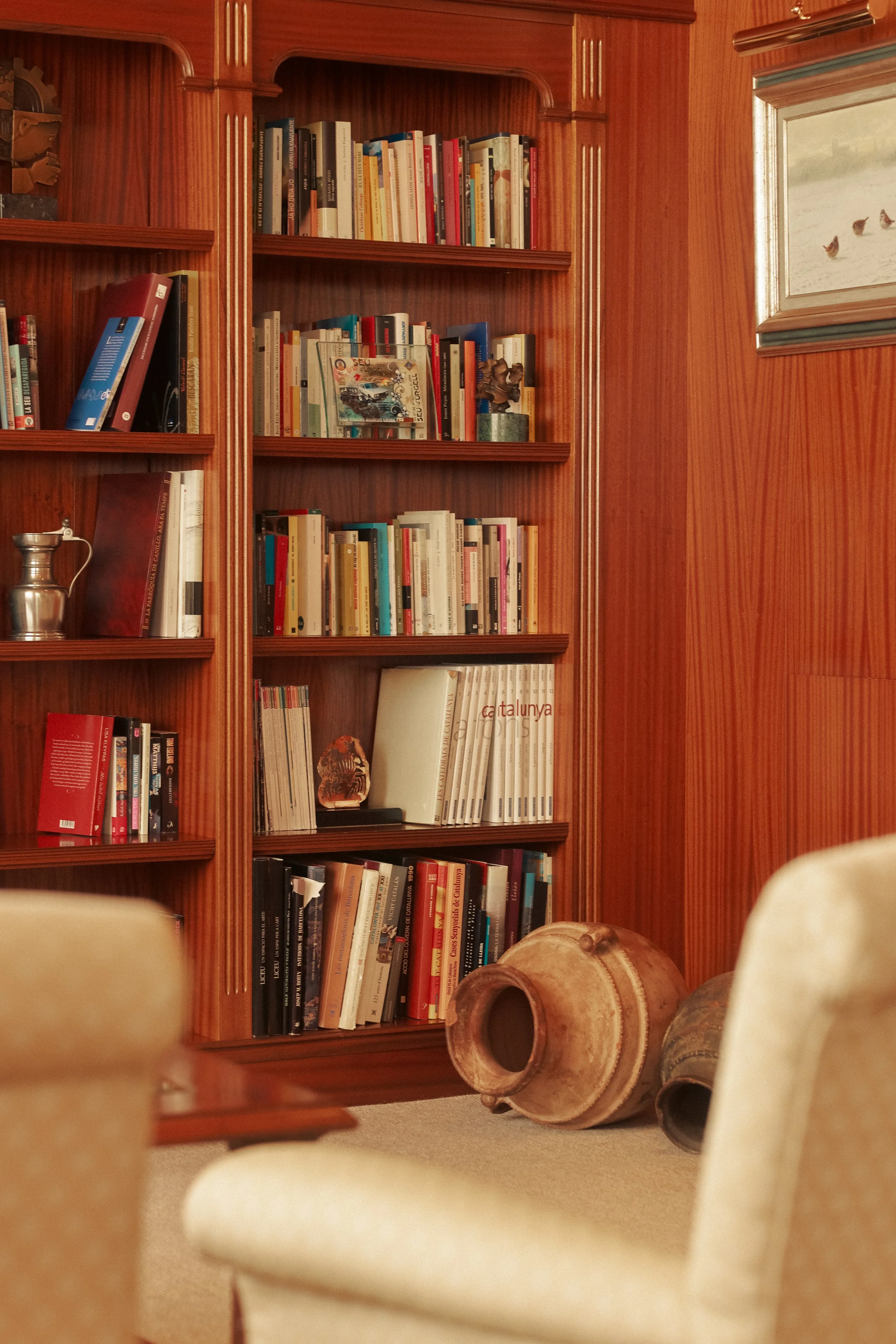 Hotel interior photography: Cozy library nook with a wooden bookshelf and cream armchair. Professional hospitality portfolio shot at El Castell de Ciutat.