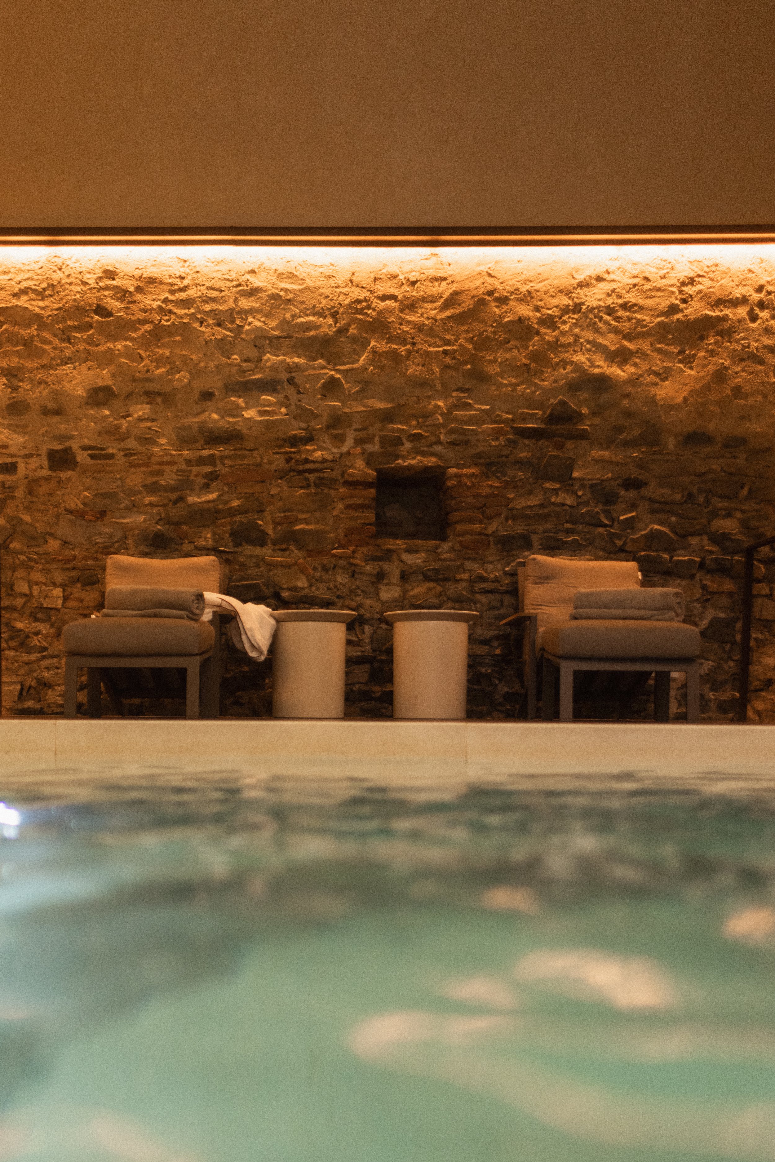 Indoor spa interior with two beige lounge chairs, rustic stone wall, and warm ambient lighting. Professional hotel spa photography for Mas d’en Bruno.