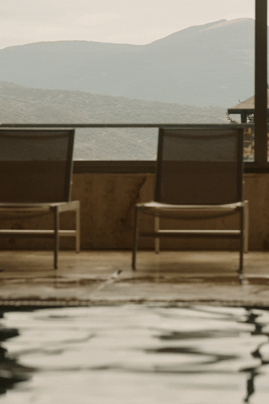 Wellness and spa photography: A guest swimming in an indoor pool with empty lounge chairs and large windows overlooking the mountains at El Castell de Ciutat. Professional hospitality portfolio imagery.