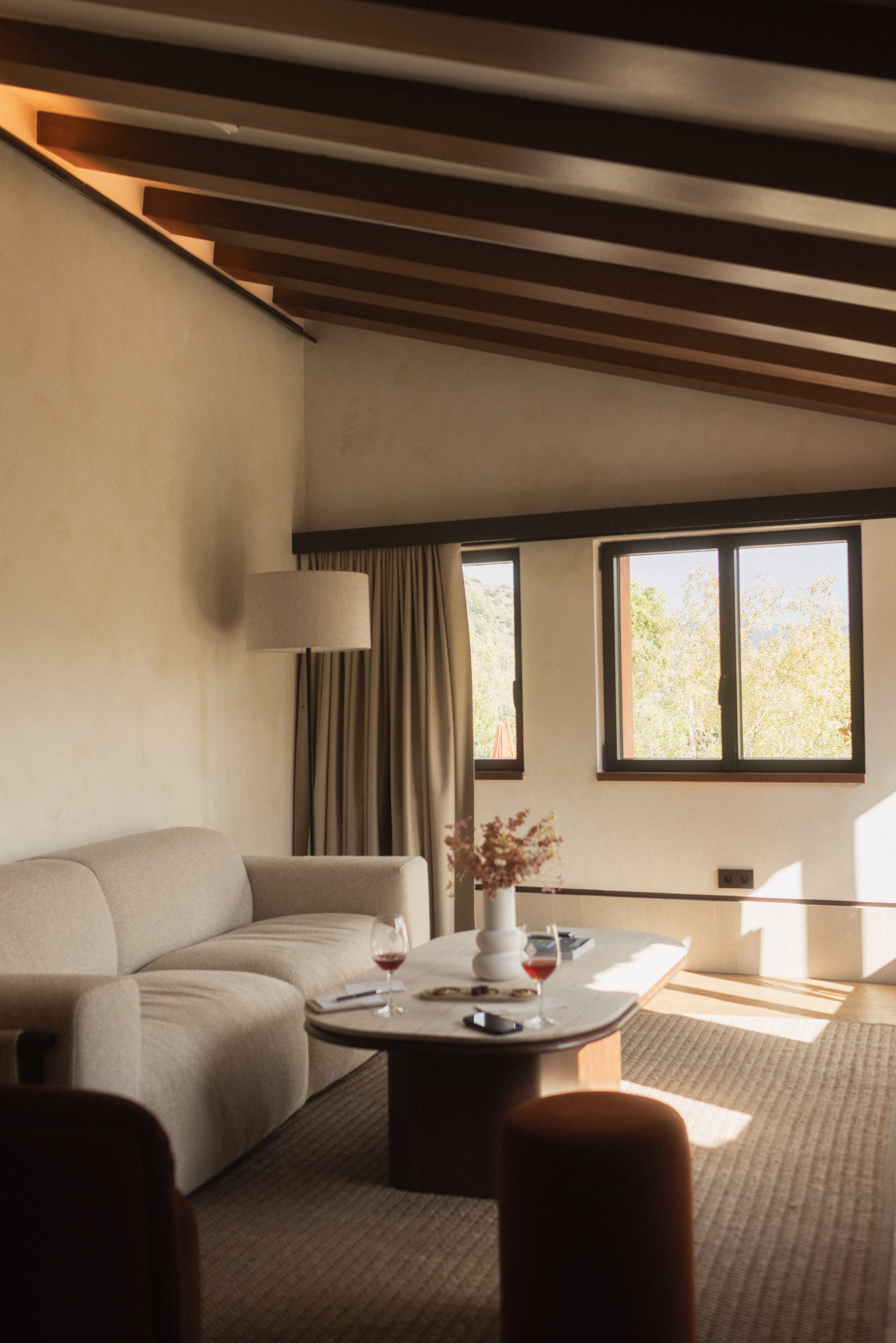 Mas d'en Bruno luxury hotel suite interior. Living room with a beige sofa, wooden ceiling beams, and red wine on a coffee table. Professional hospitality photography by Valerie.