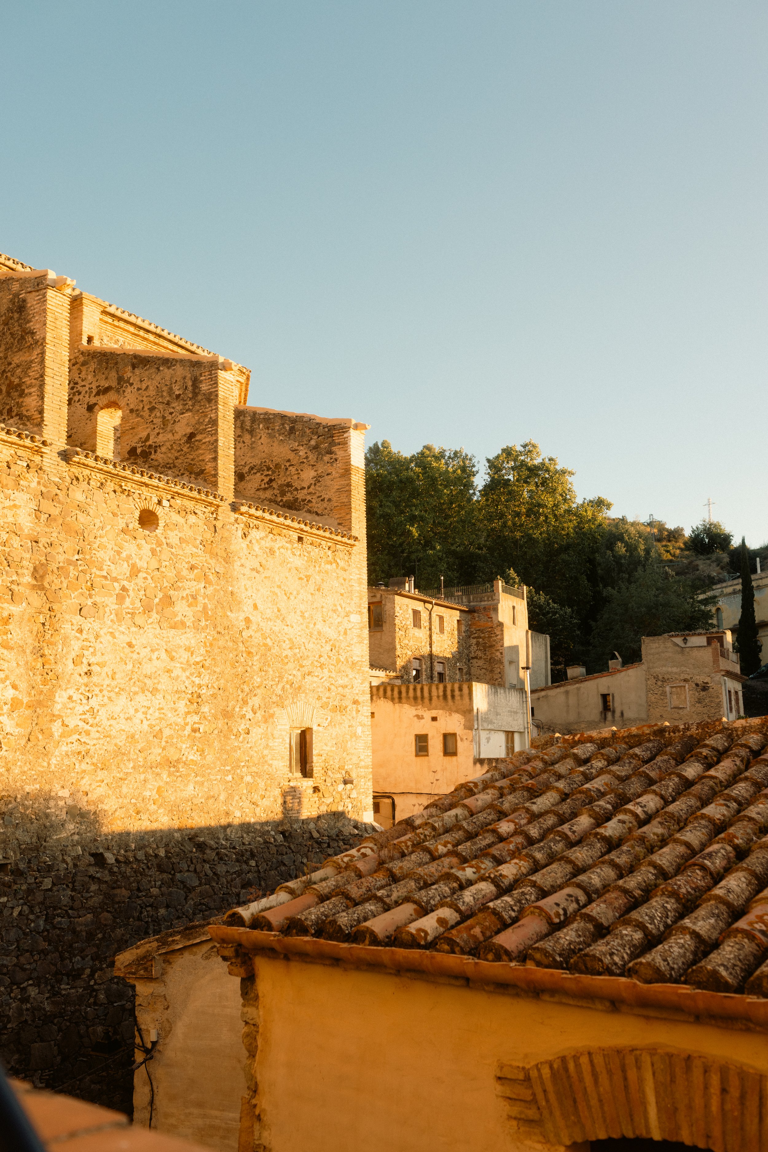 Sunlit view of ancient stone buildings with terracotta roofs in a Catalan village nestled within the Priorat vineyard landscape. Professional hotel and travel photography at Ora Priorat.