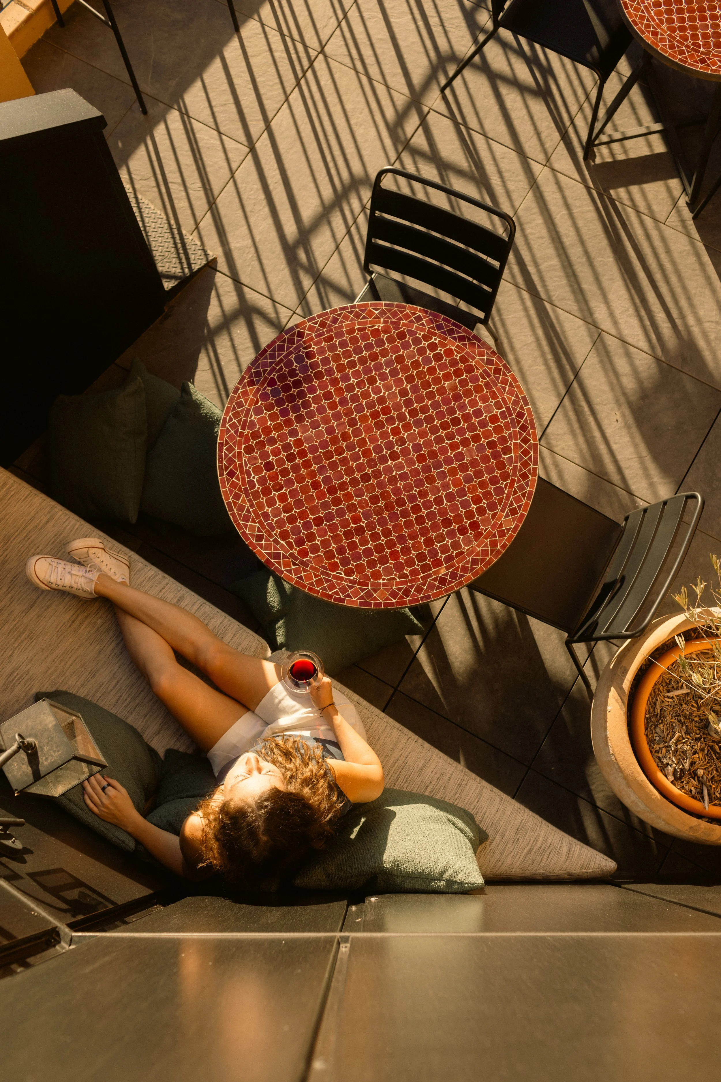 Lifestyle hospitality photography: overhead shot of a guest relaxing on a patio with red wine. Professional hotel courtyard and exterior furniture styling at Ora Priorat.