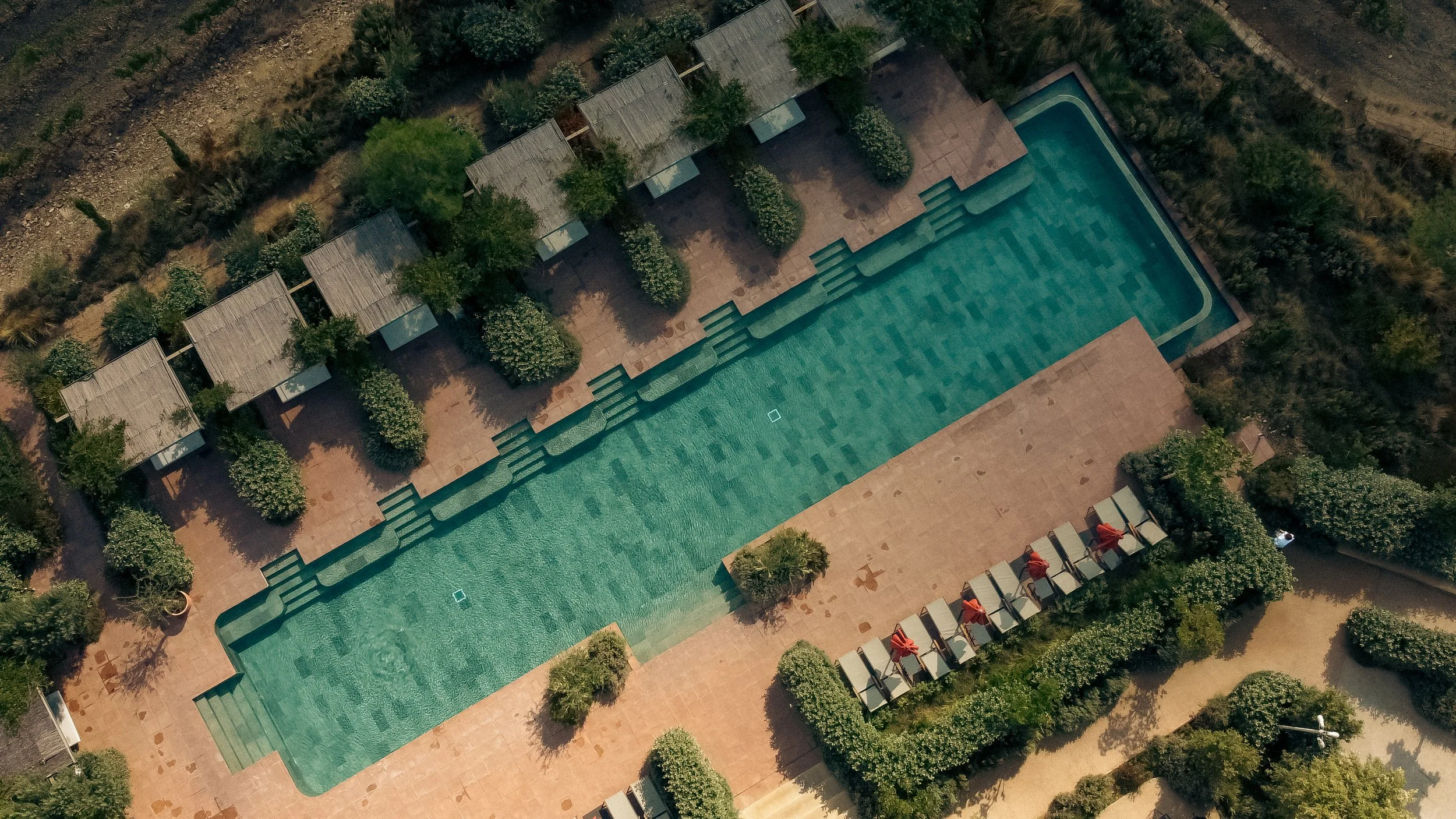 Mas d’en Bruno hotel pool and grounds, aerial view with sun loungers, umbrellas and surrounding greenery, Catalonia, Spain.