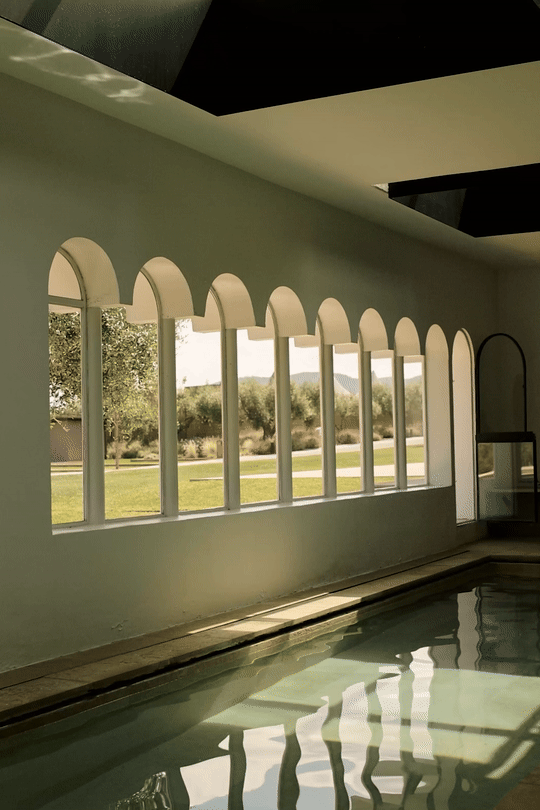 Cinematic indoor wellness pool at Font de la Canya: arched windows with a dynamic view of the Mediterranean landscape.