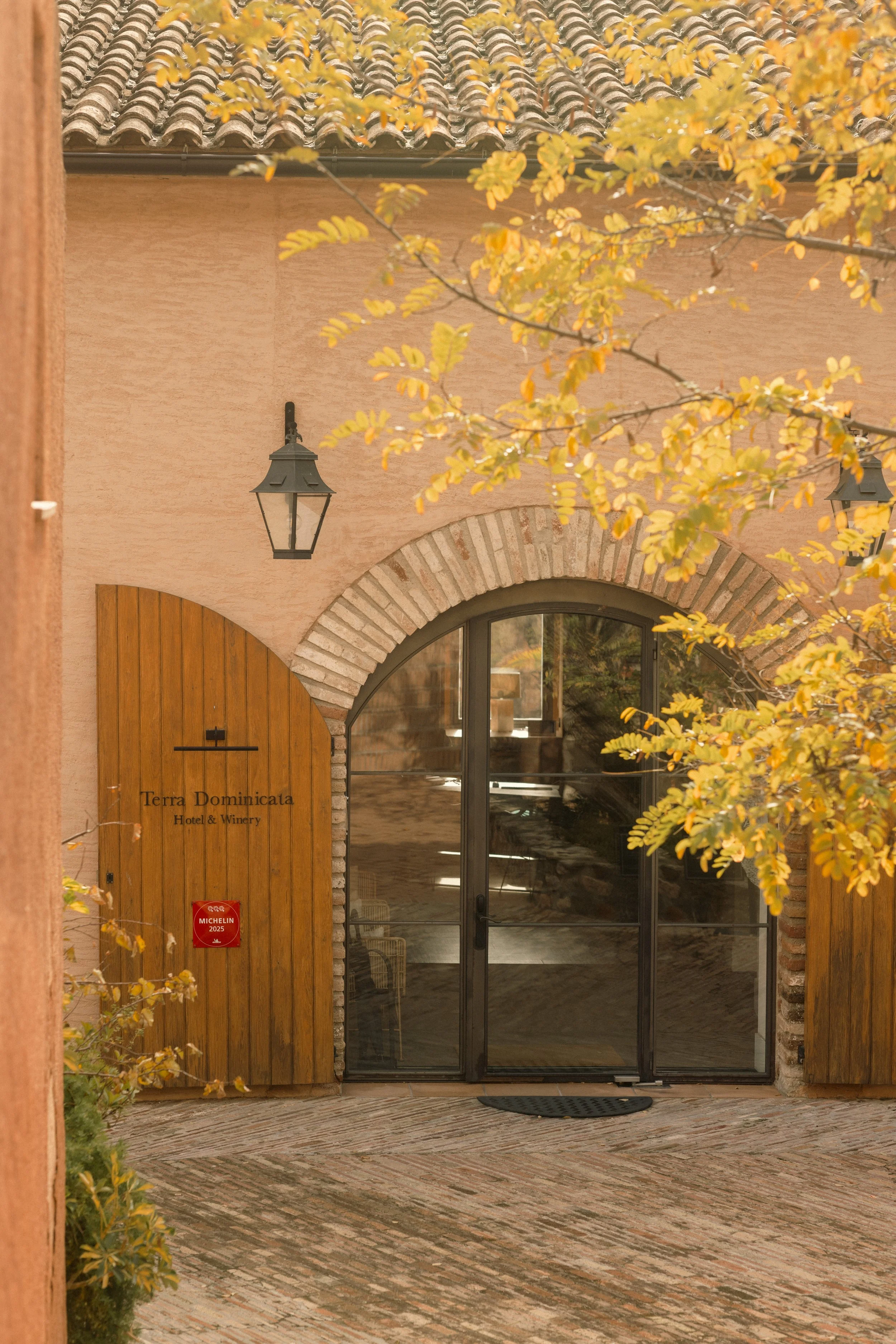 Luxury boutique arrival at Terra Dominicata: illuminated arched entrance surrounded by the seasonal colors of Priorat.