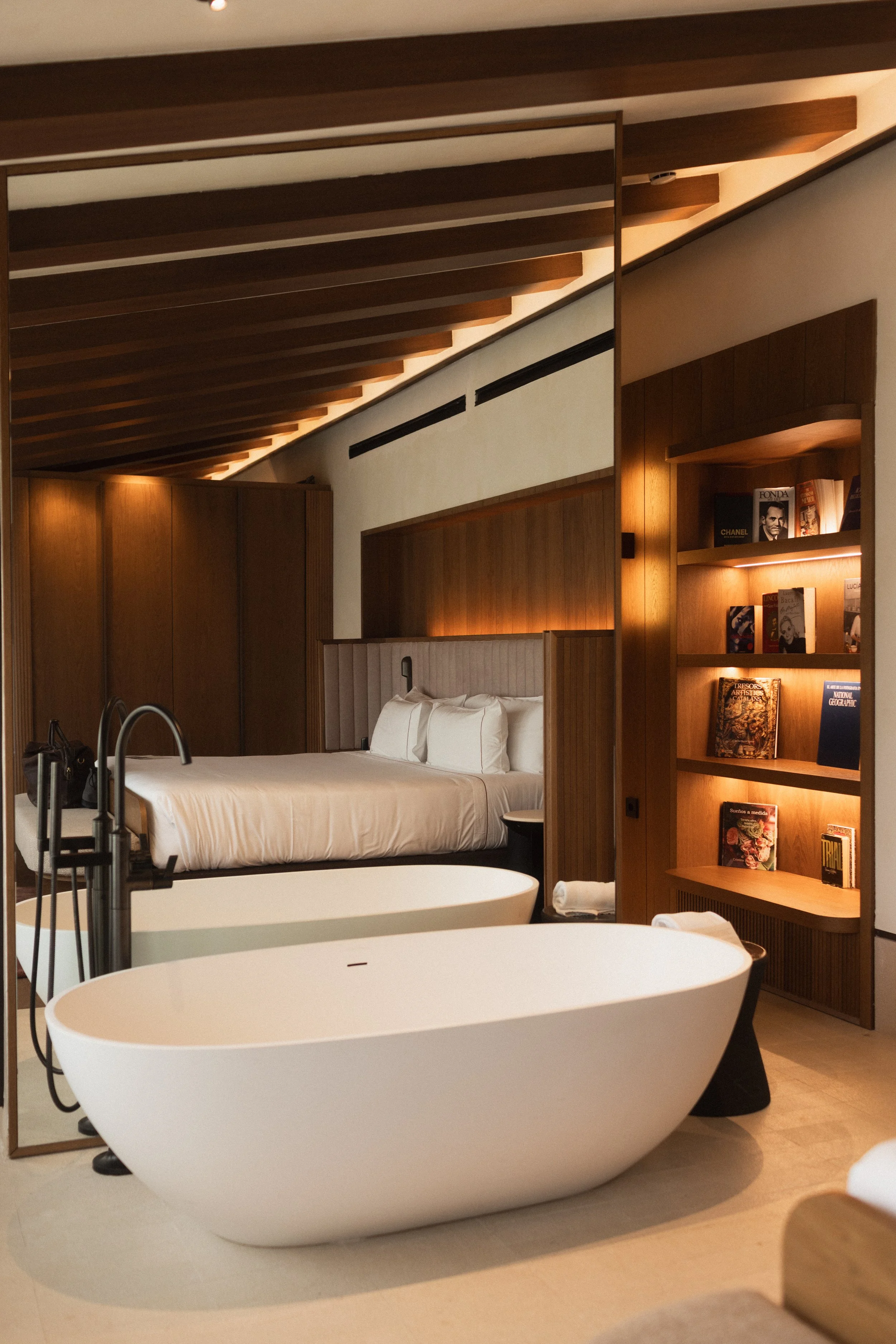 Mas d'en Bruno luxury hotel suite interior. Freestanding bathtub, bed with white linens, and a wooden bookshelf with warm lighting. Hospitality interior photography by Valerie.