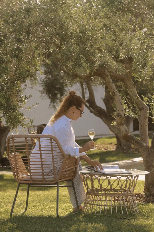 Cinematic lifestyle GIF at Font de la Canya: guest relaxing with white wine and a magazine in a Mediterranean garden lounge.