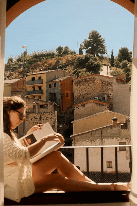 A candid shot of a guest reading on a room balcony with a scenic mountain view in the Priorat region. Example of natural light hospitality imagery.