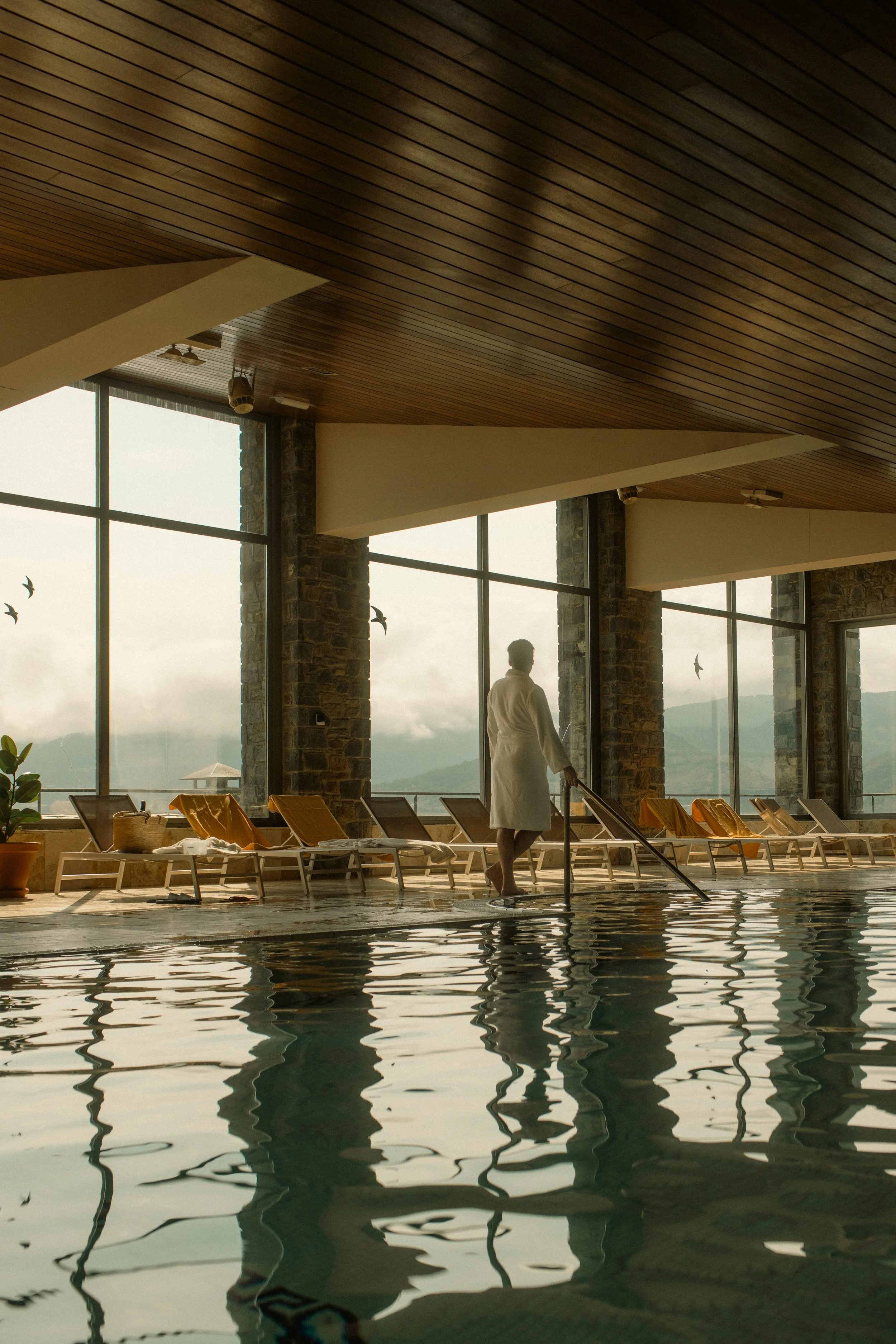 Wellness and spa photography: Indoor pool area with staff service, wooden ceiling, and mountain views at El Castell de Ciutat. Professional hospitality portfolio shot.