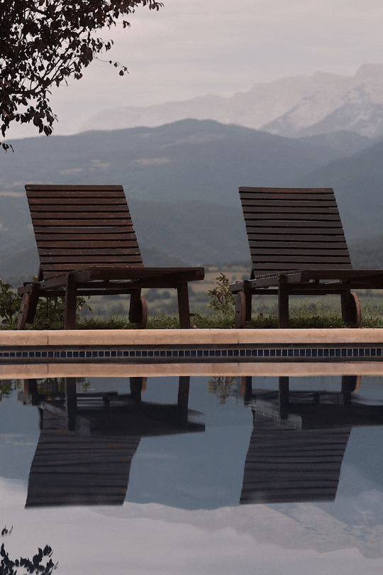 Wellness and spa photography: Animated GIF of a mountain reflection in an outdoor pool with wooden lounge chairs. Atmospheric hospitality imagery at El Castell de Ciutat.