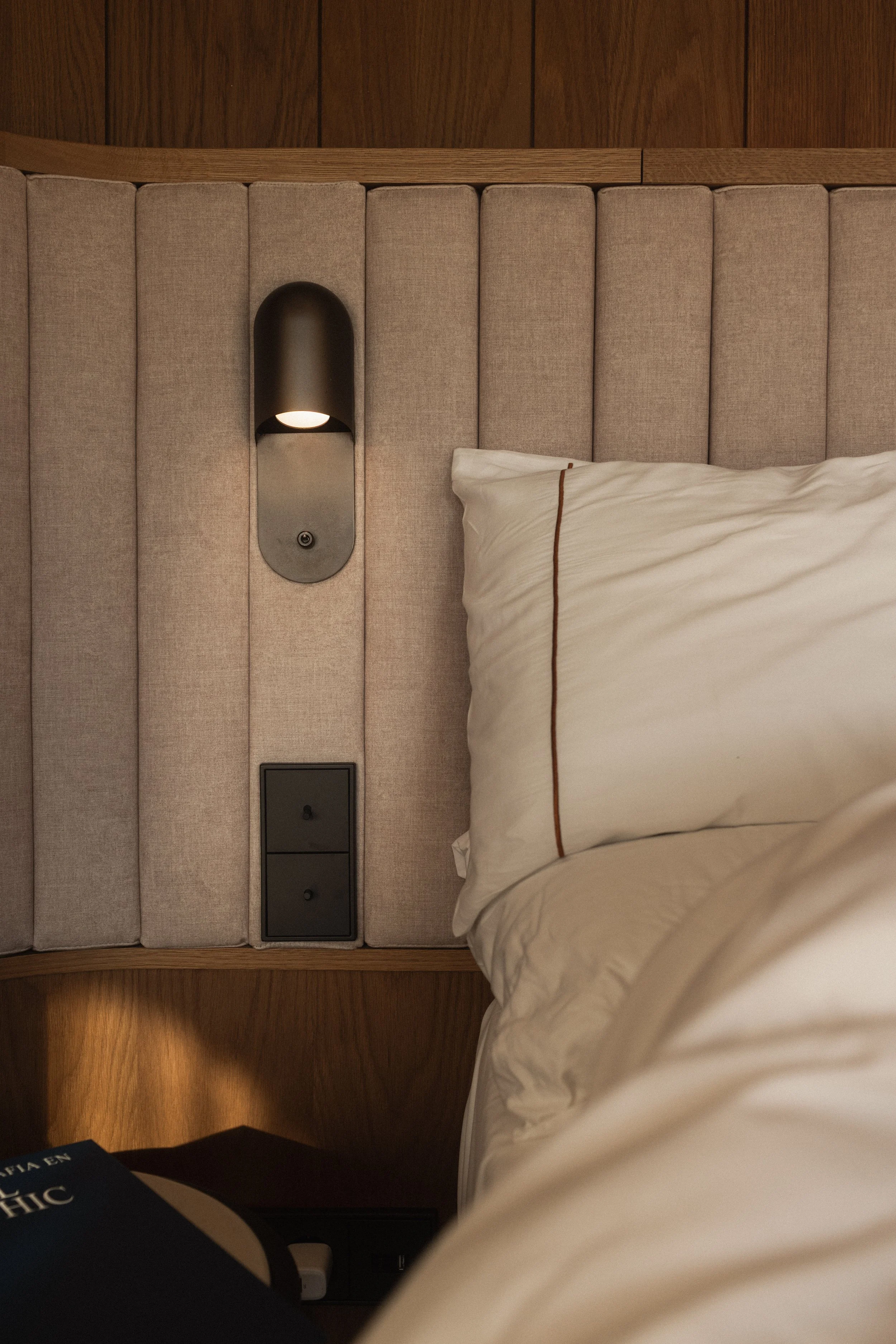 Mas d’en Bruno hotel room with upholstered headboard, reading light and bedside details, Catalonia, Spain.